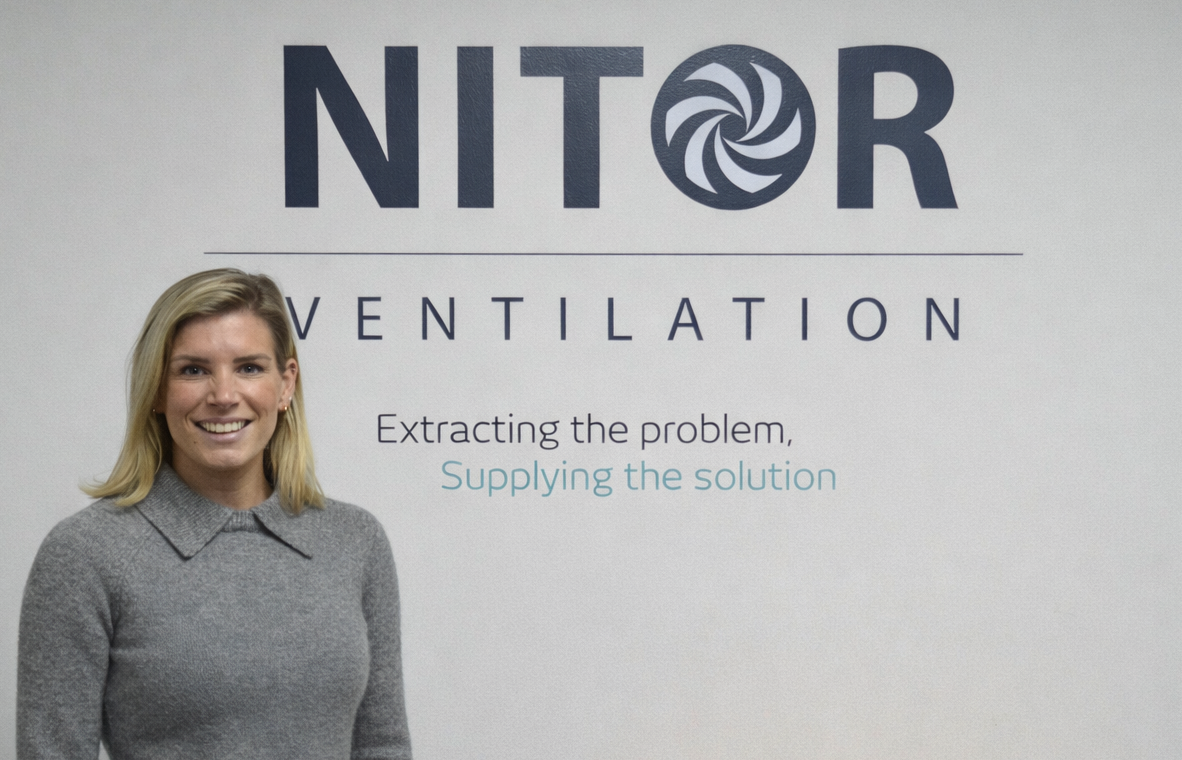 Woman in gray sweater standing in front of NITOR VENTILATION logo.