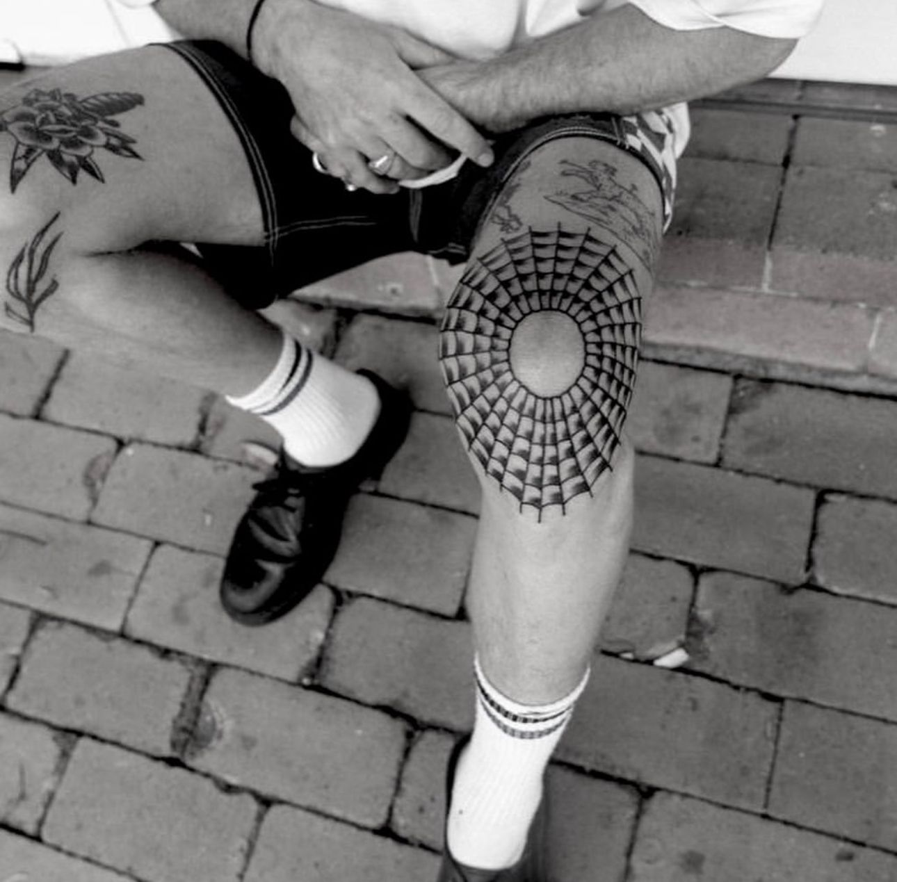 Person with knee tattoo and other leg tattoos, sitting on brick steps, wearing shorts and socks.