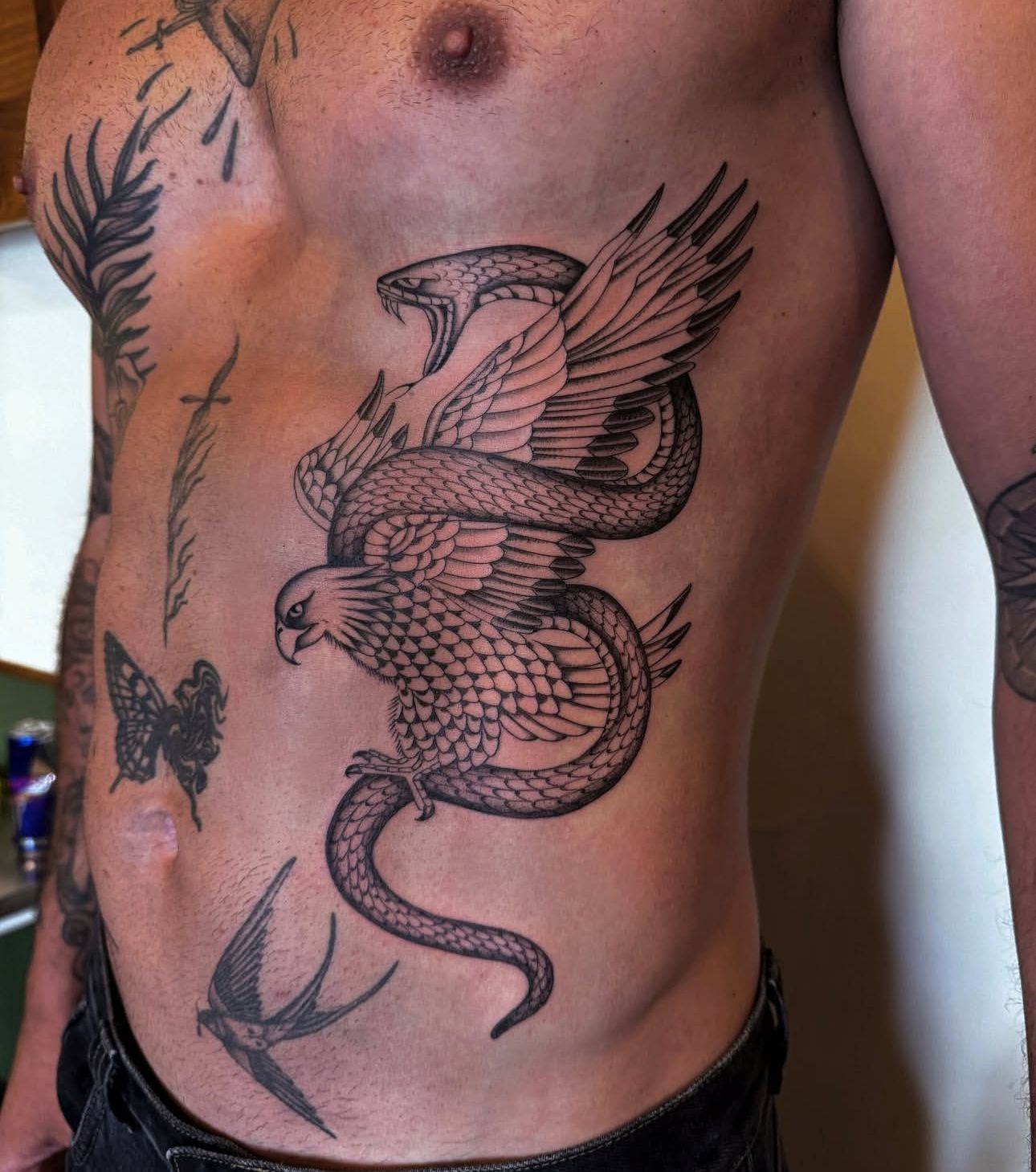 Man's torso tattoo of eagle fighting a snake, with other small tattoos.