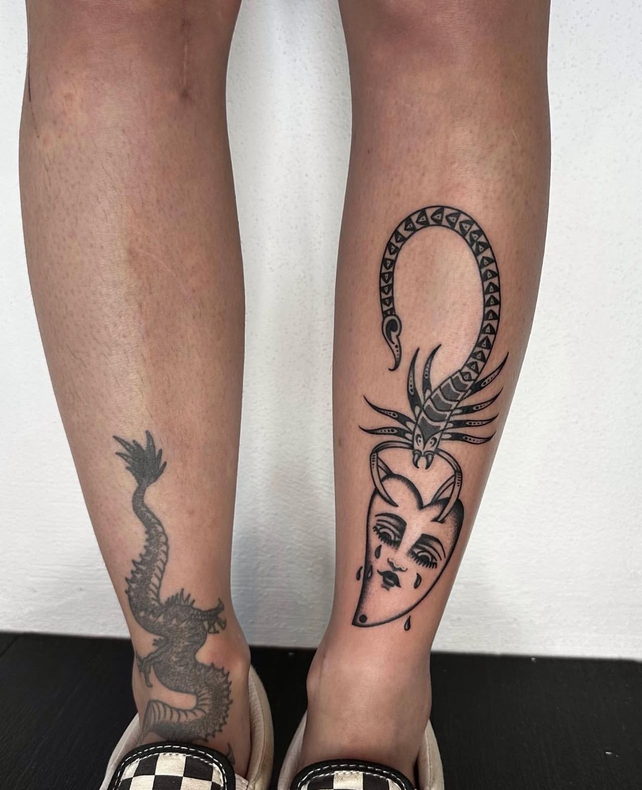Two legs with tattoos: Dragon on one ankle, snake and crying mask on the other.