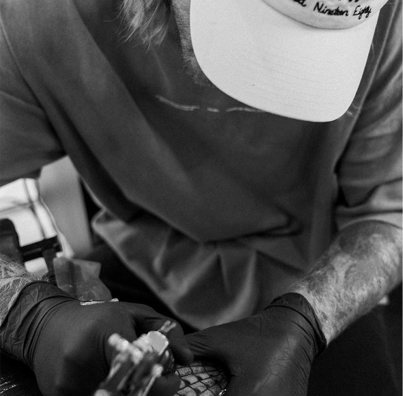 Person wearing gloves, tattooing; hands holding a tattoo gun, close-up.