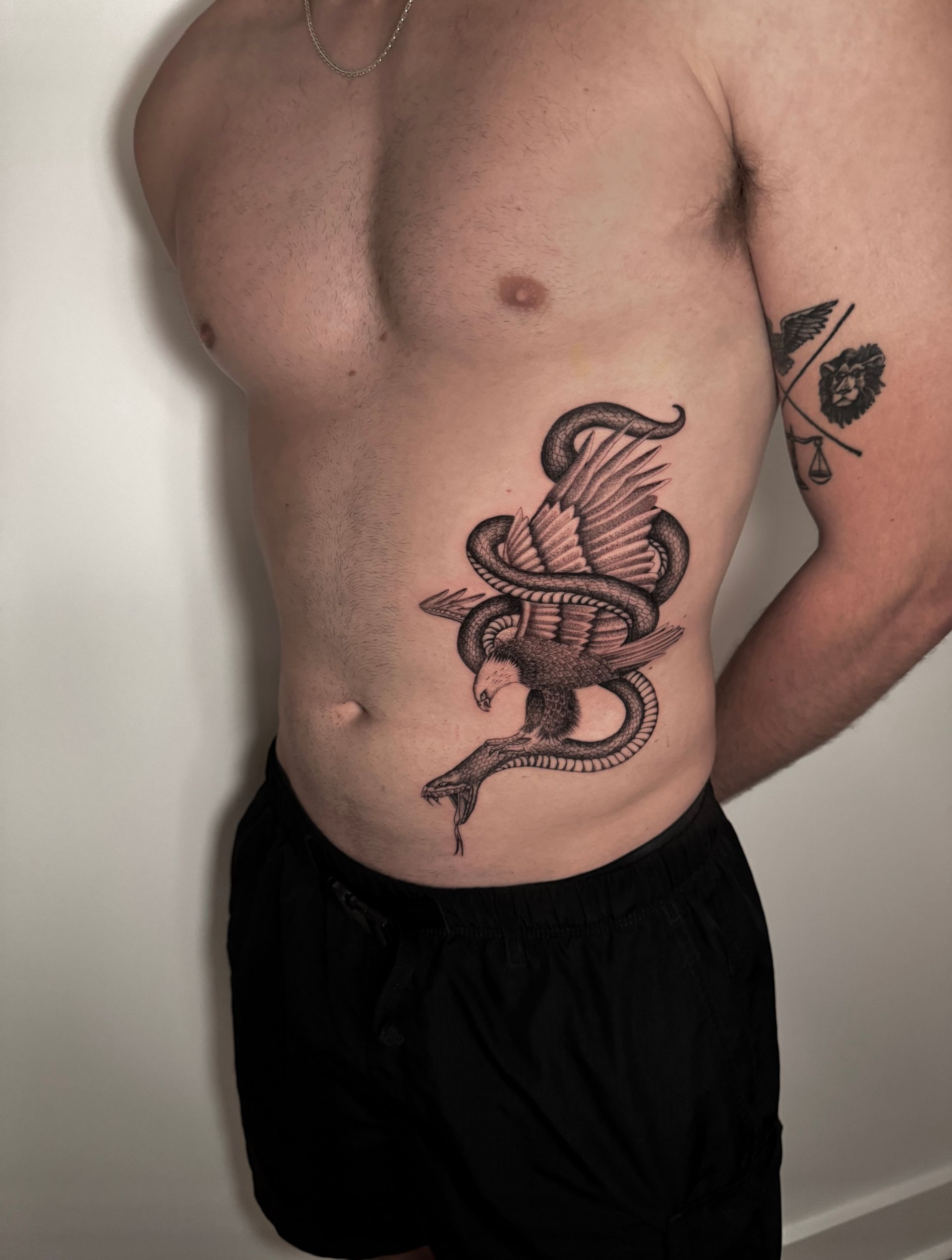 Man with torso tattoo of a snake coiled around a bird, wearing black shorts.