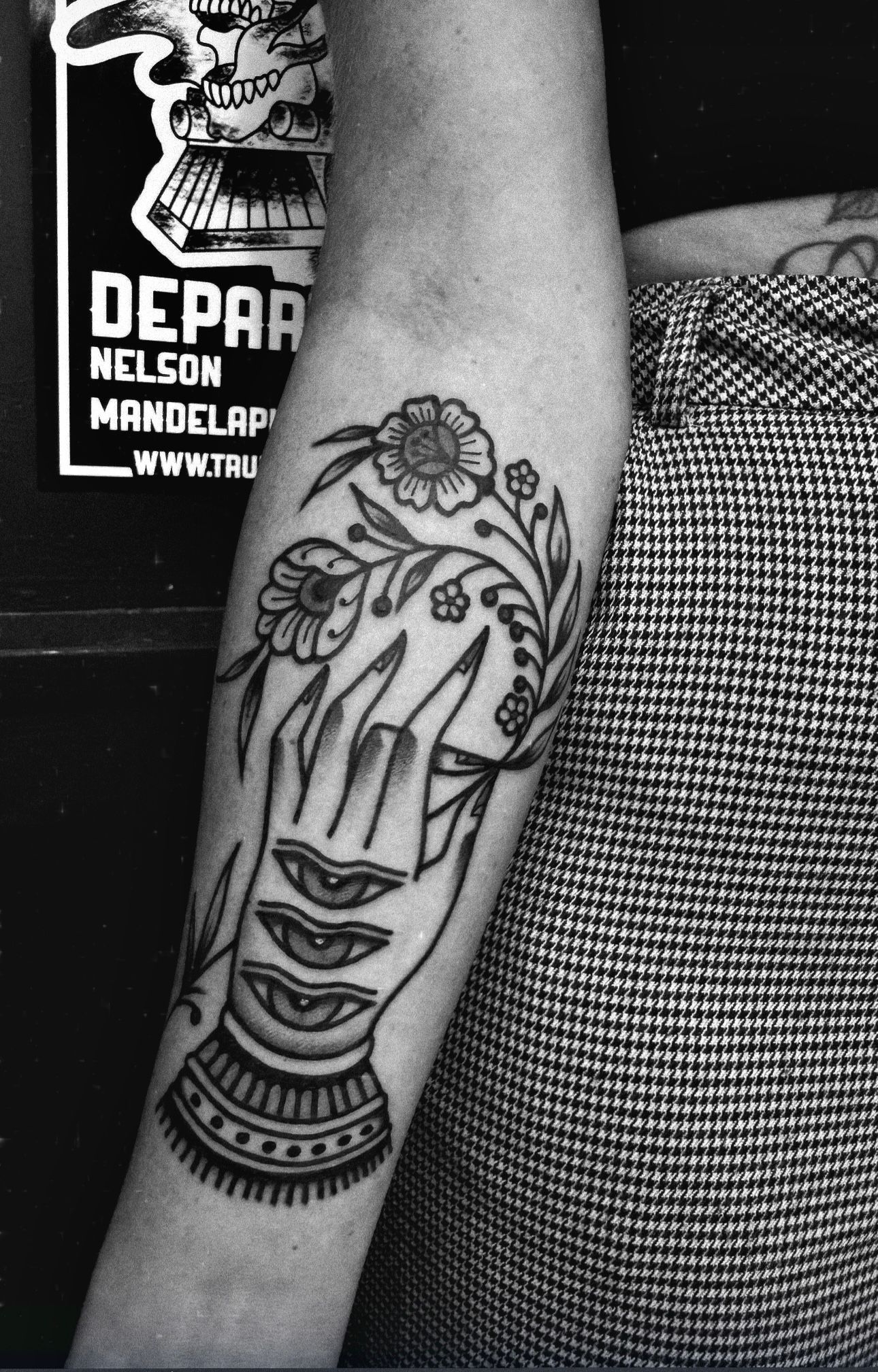 Black and white tattoo on an arm: a hand with sliced mouths and floral elements.