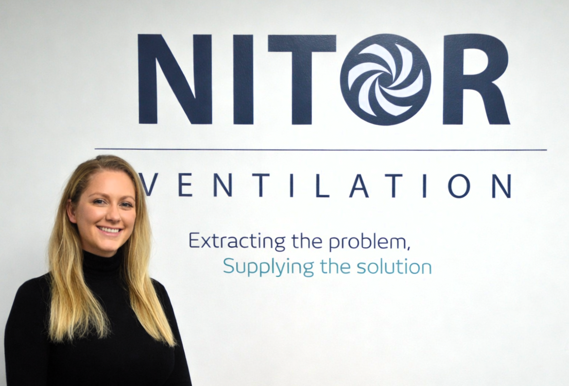 Woman smiles in front of a wall with the NITOR VENTILATION logo and slogan.