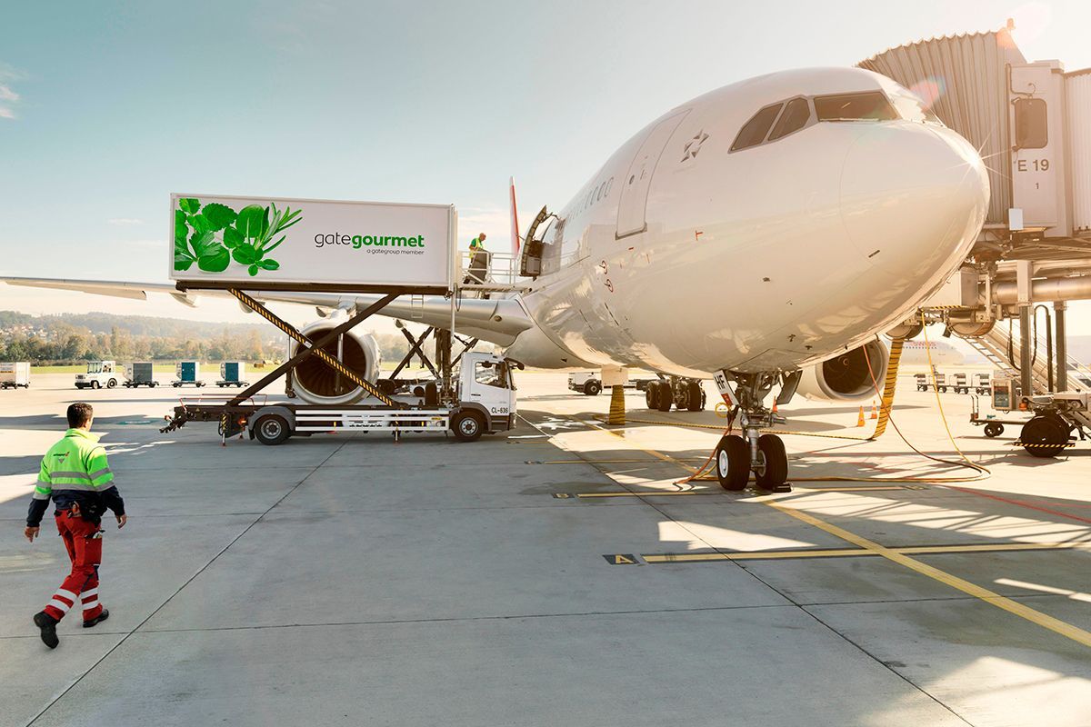 A cargo truck loading a container onto an airplane at an airport. A worker walks nearby.