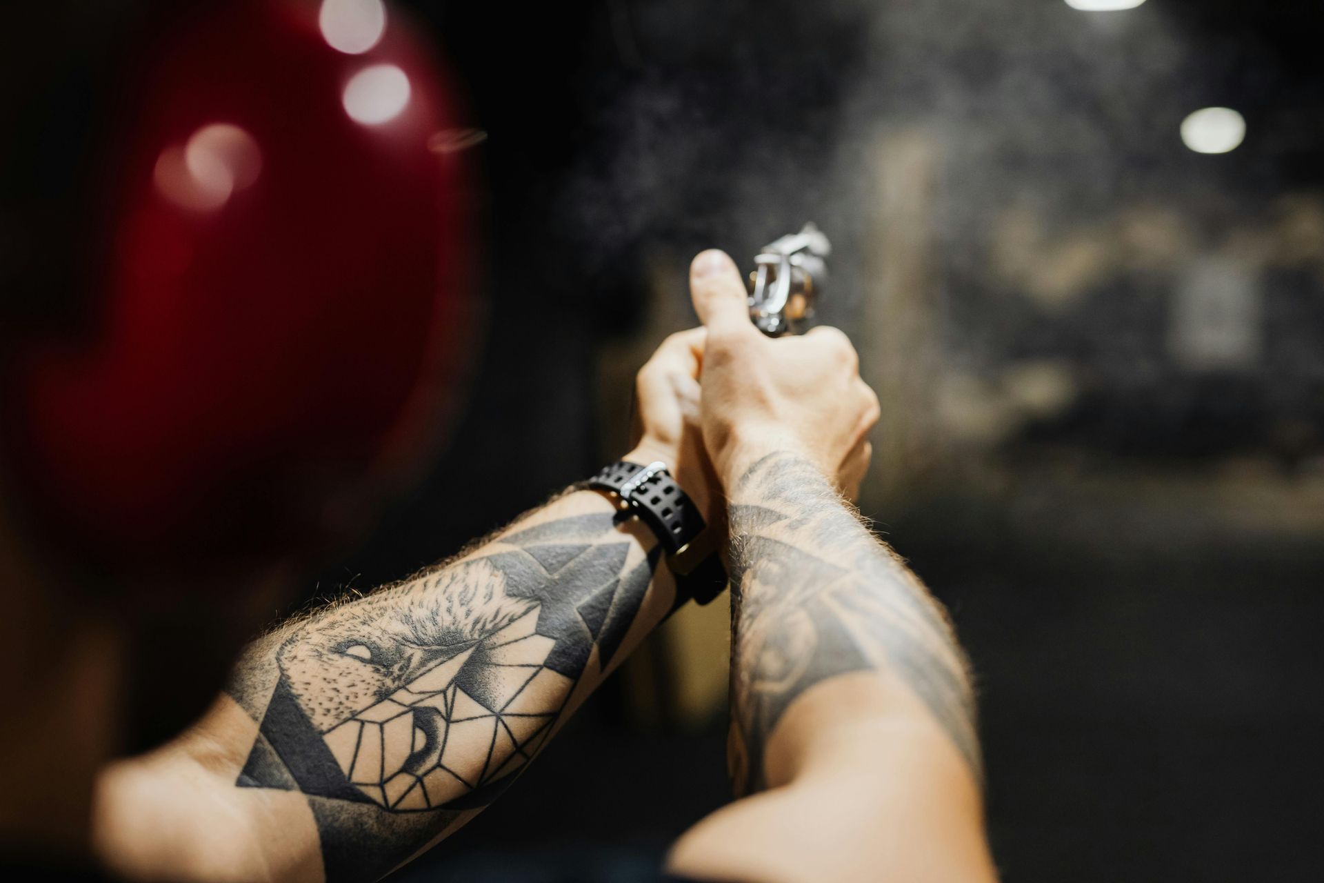 Person's tattooed arms holding a spray bottle, misting into the air near a red balloon.