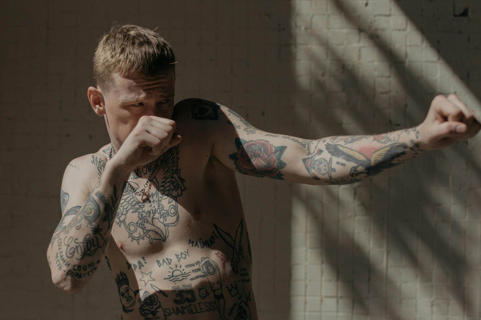 Man with tattoos throws a punch, sunny setting.
