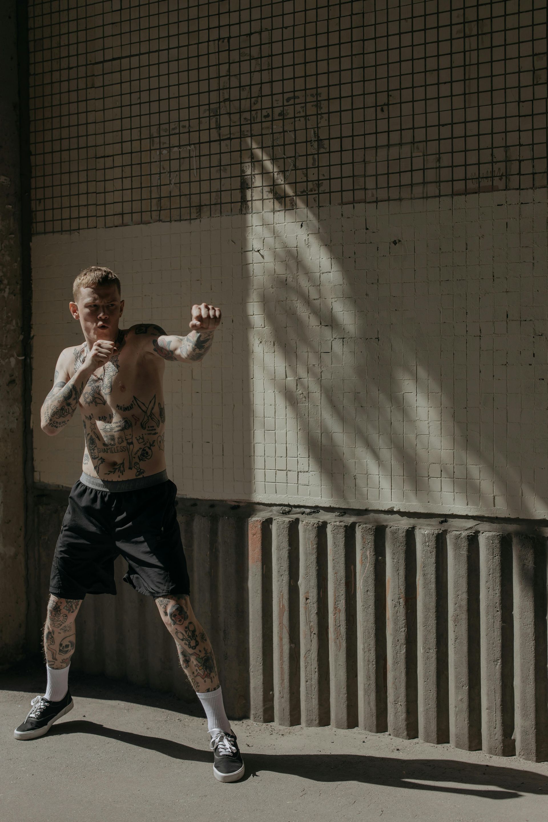 Man with tattoos shadow boxing in an urban setting. He's wearing black shorts and socks.