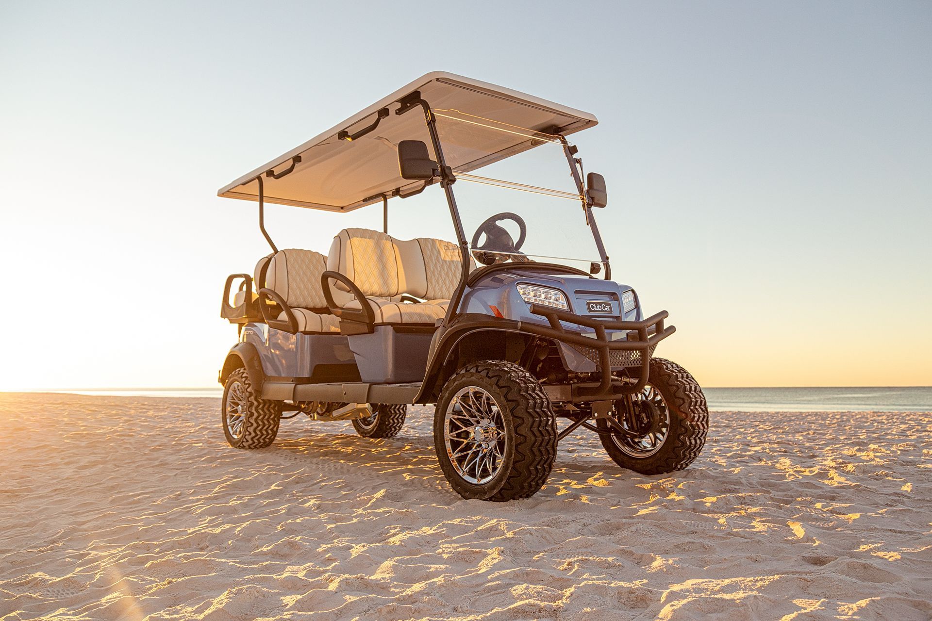 A golf cart is parked on the beach at sunset.
