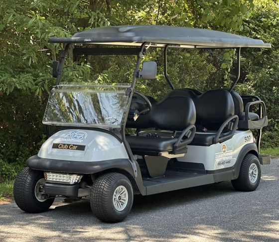 A white golf cart with black seats is parked on the side of the road.