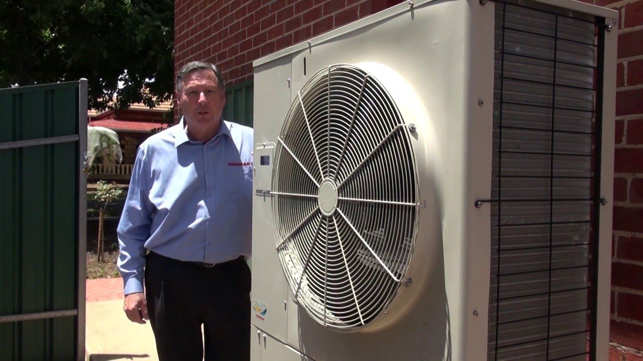 A man is standing next to a large fan on the side of a building.