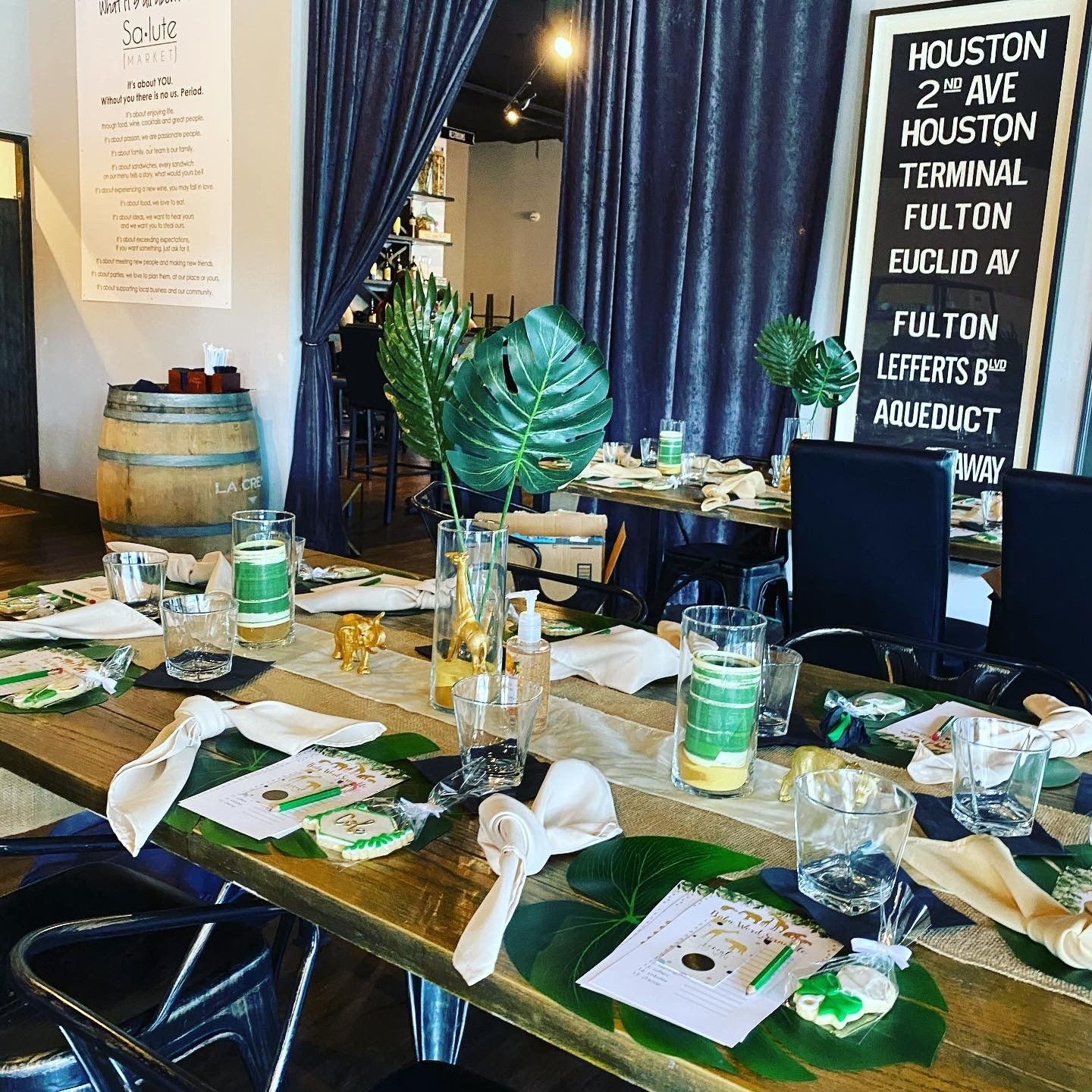 A long table with plates , glasses , and leaves on it in a restaurant.