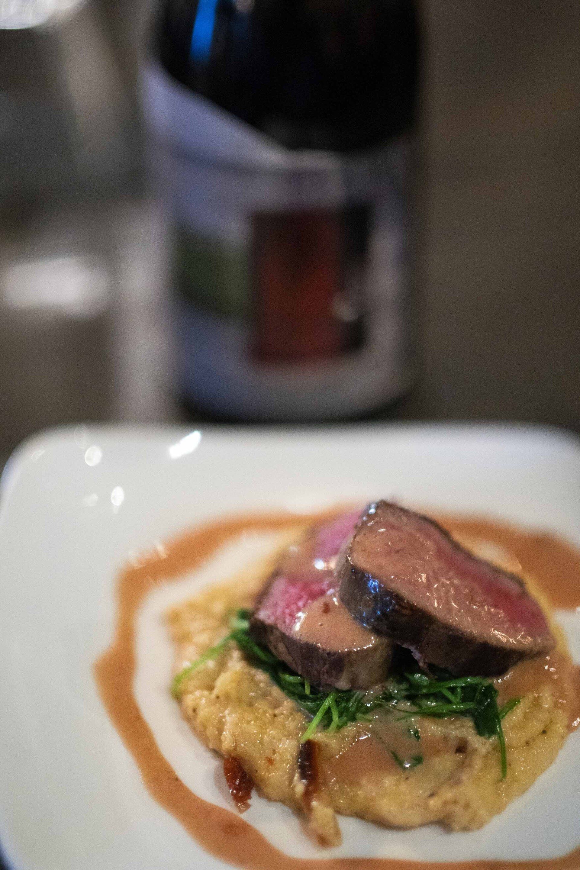 A close up of a plate of food with a bottle of wine in the background.