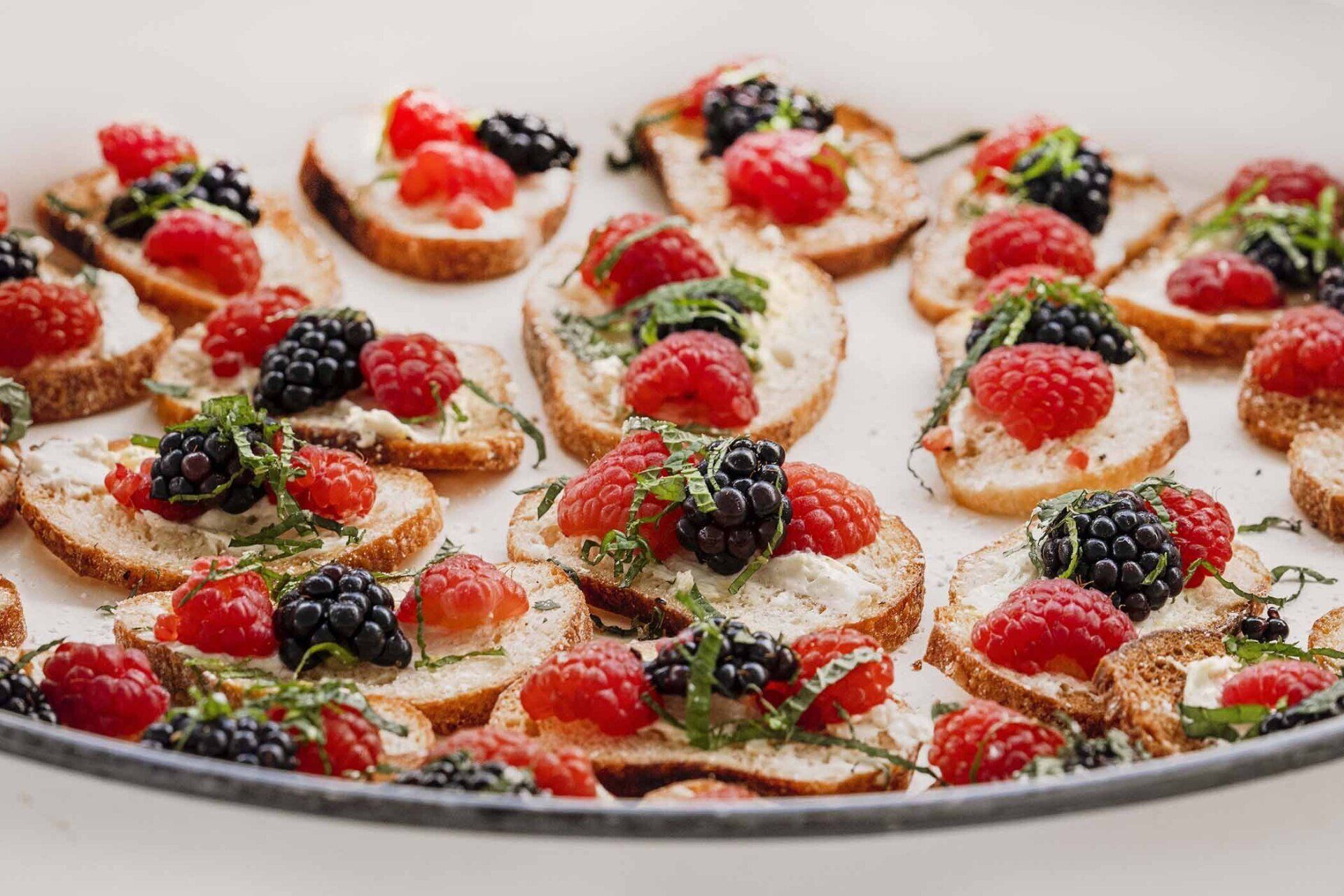 A tray of appetizers with raspberries and blackberries on bread.