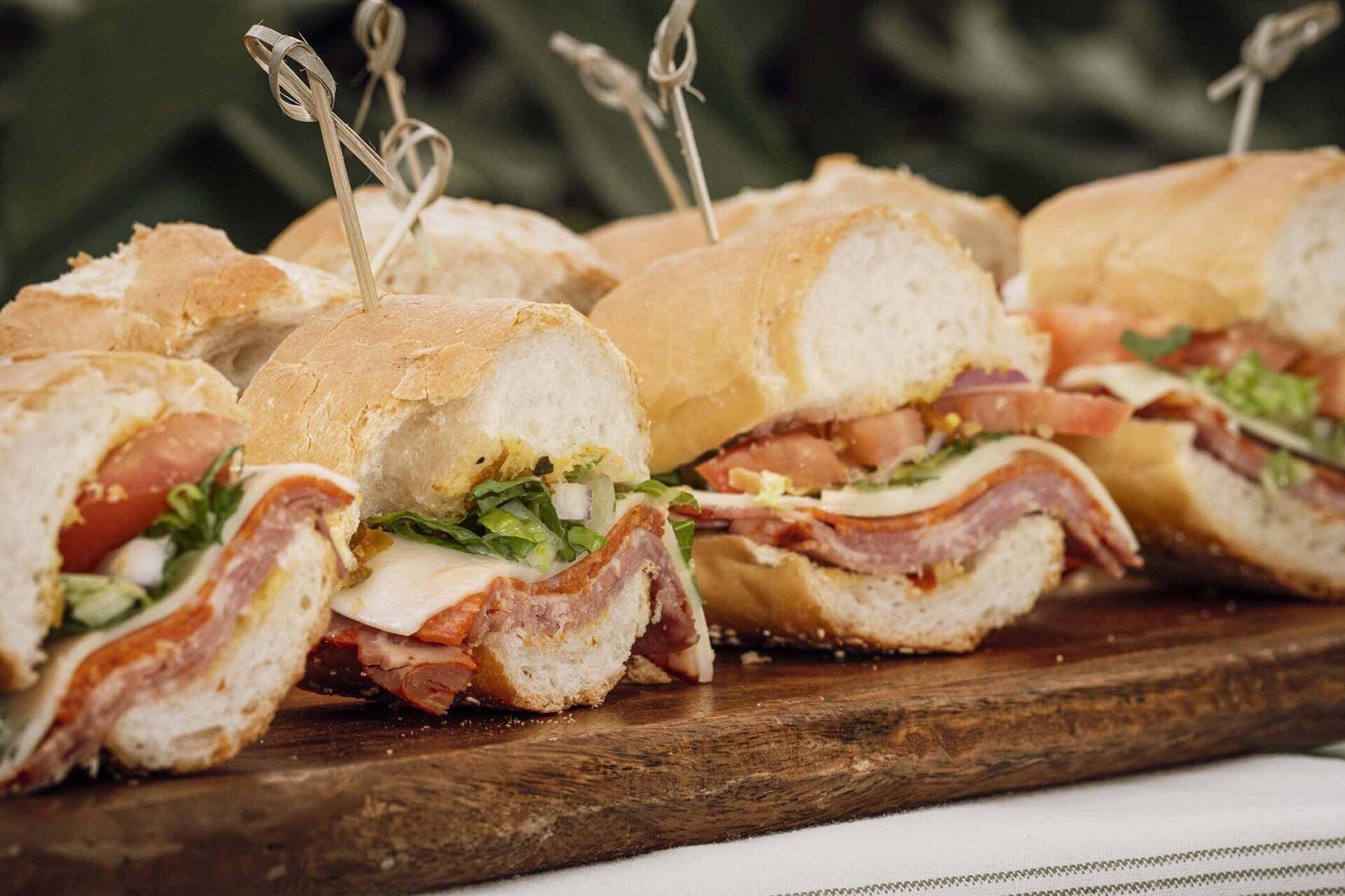 A row of sandwiches sitting on top of a wooden cutting board.