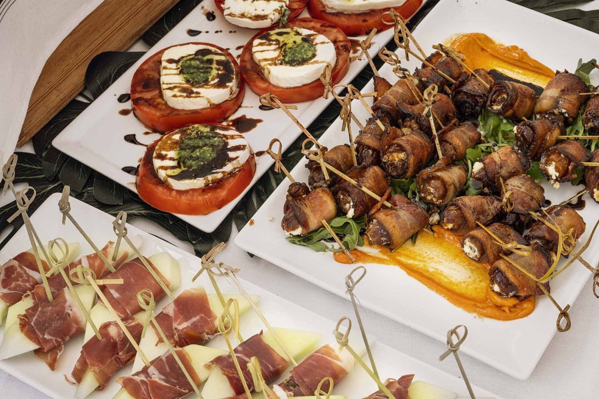 A table topped with plates of food including bacon wrapped dates and tomatoes