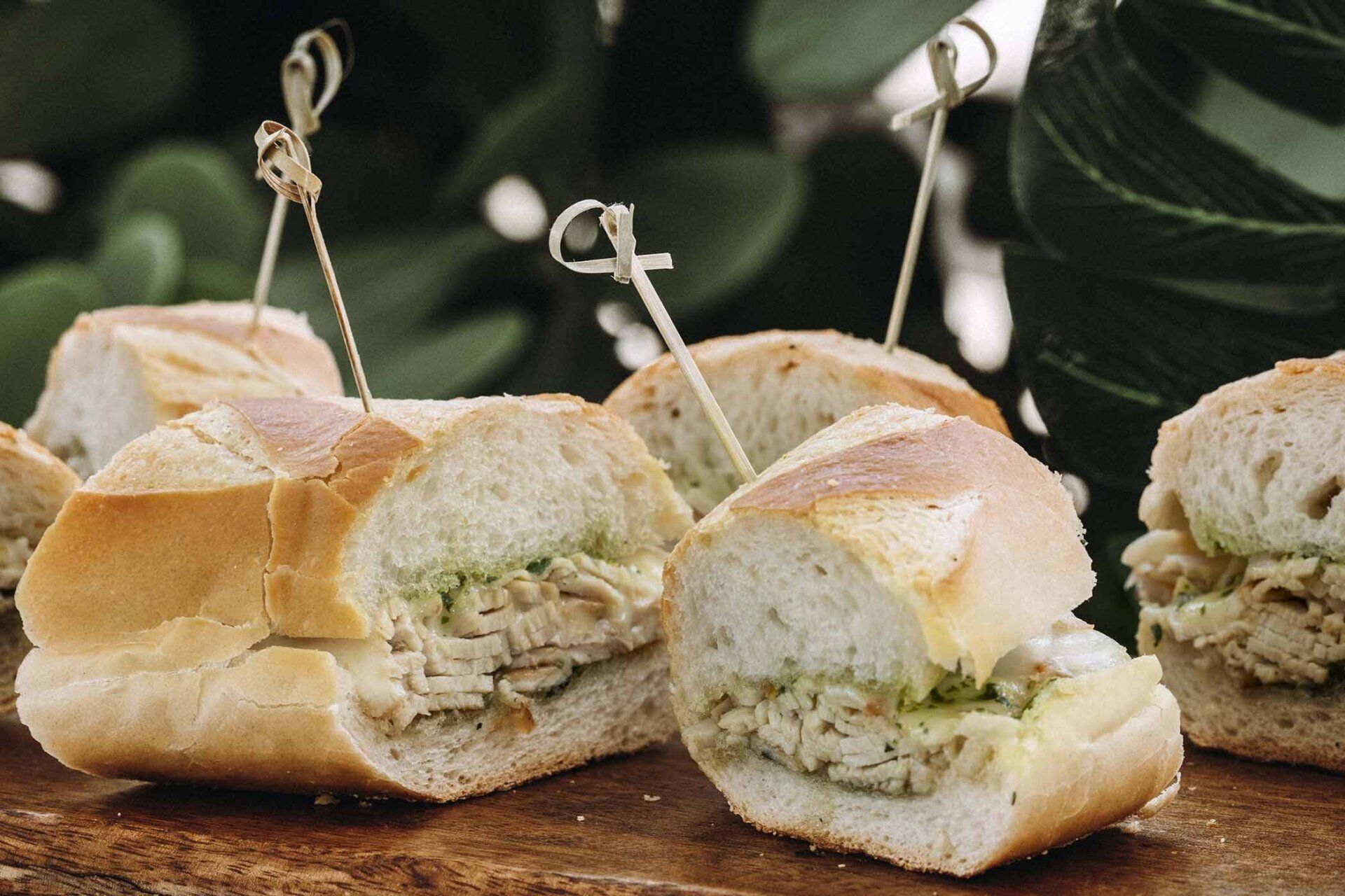 A bunch of sandwiches with toothpicks in them on a wooden table.