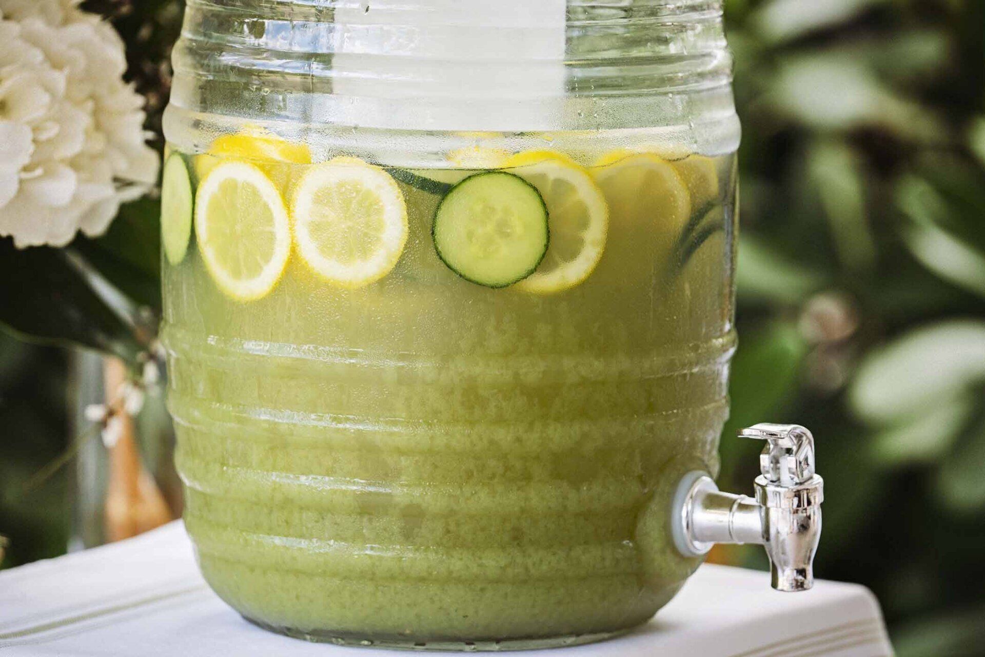 A beverage dispenser filled with green liquid and lemon slices.