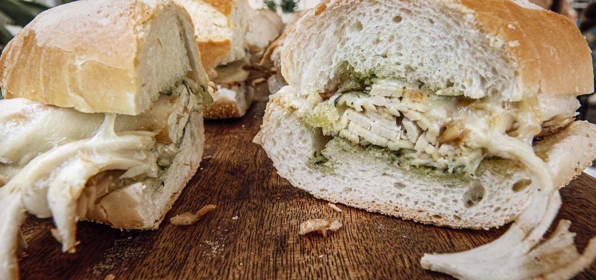 A sandwich is cut in half on a wooden cutting board.