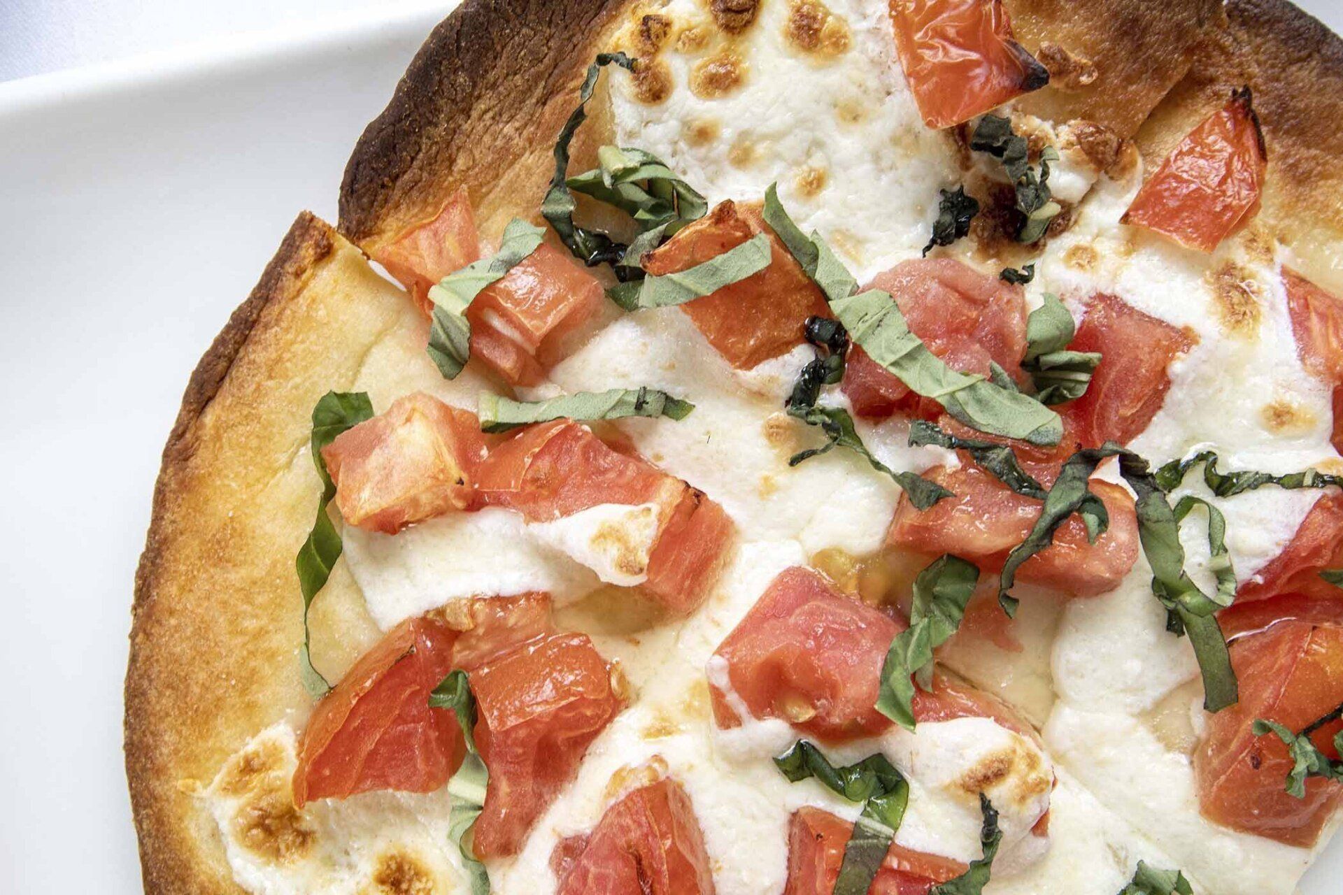A pizza with tomatoes and basil on a white plate