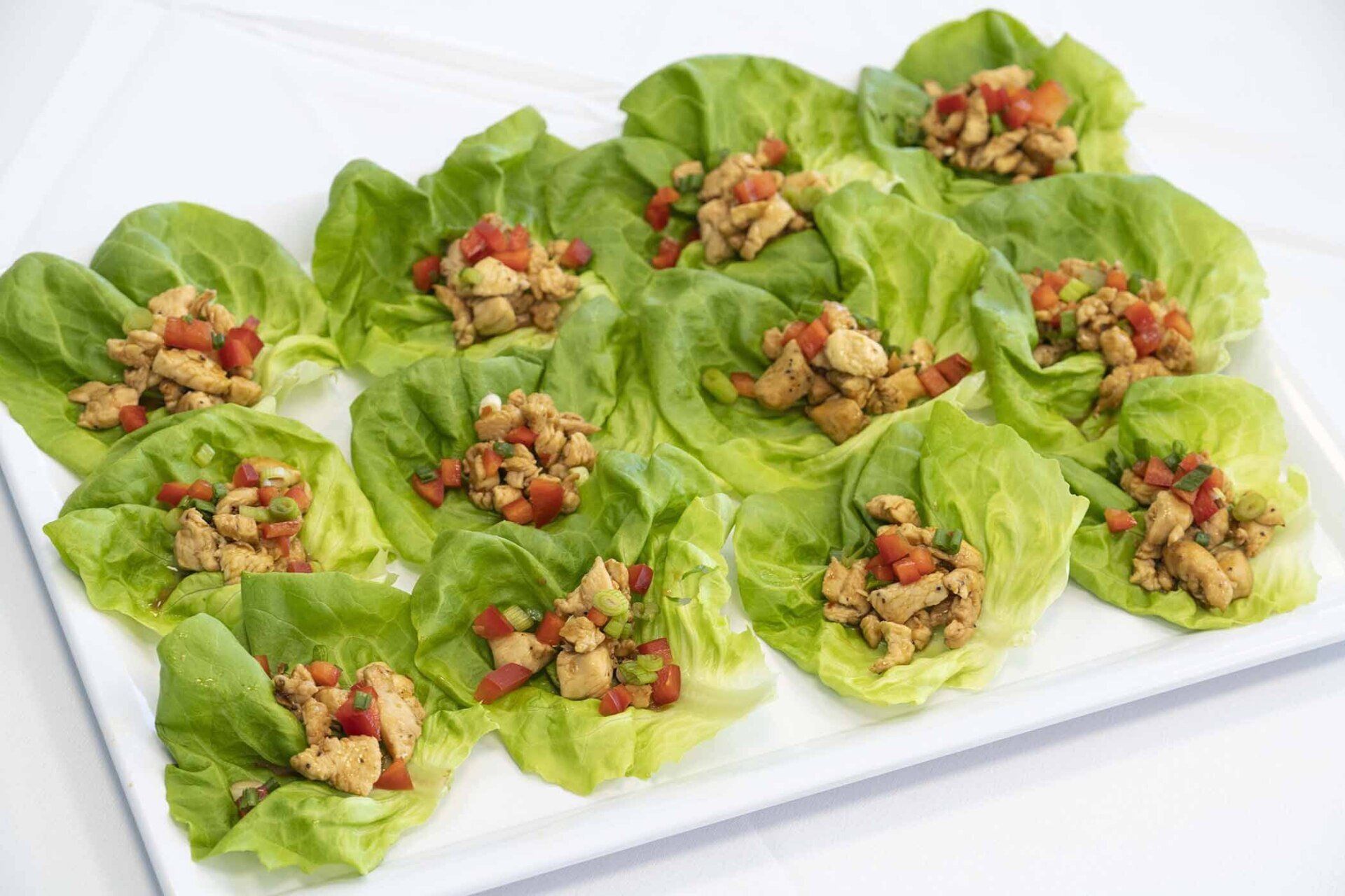 A white plate topped with lettuce wraps filled with chicken and tomatoes.