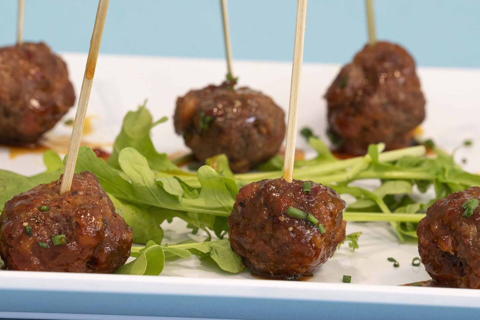 A white plate topped with meatballs and lettuce on toothpicks.