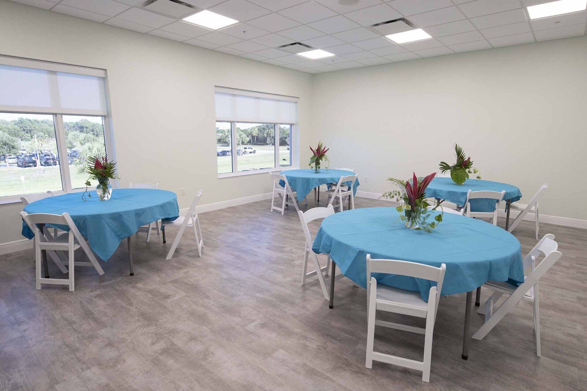 A room filled with tables and chairs with blue tables and white chairs.