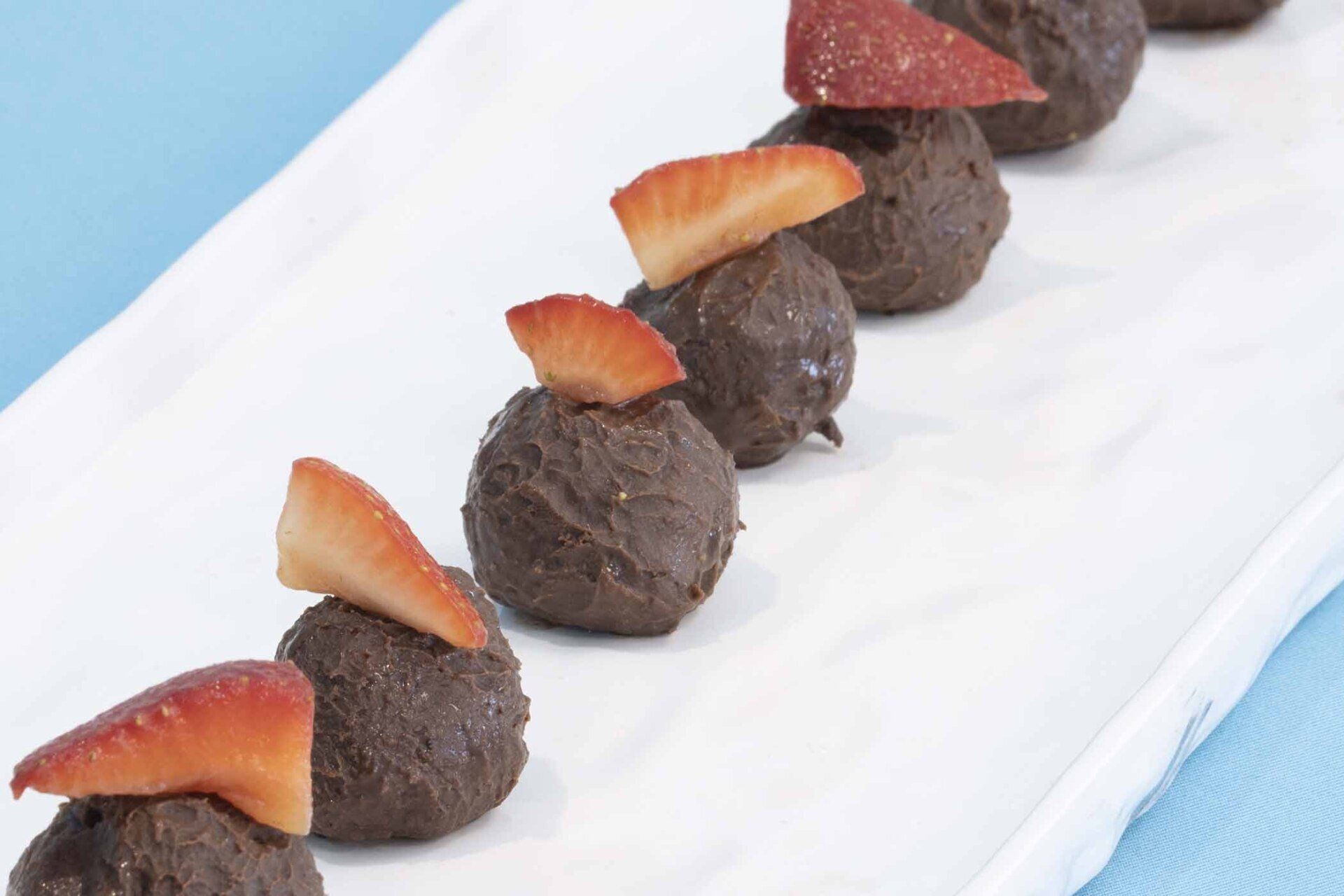 A white plate topped with chocolate balls and strawberries
