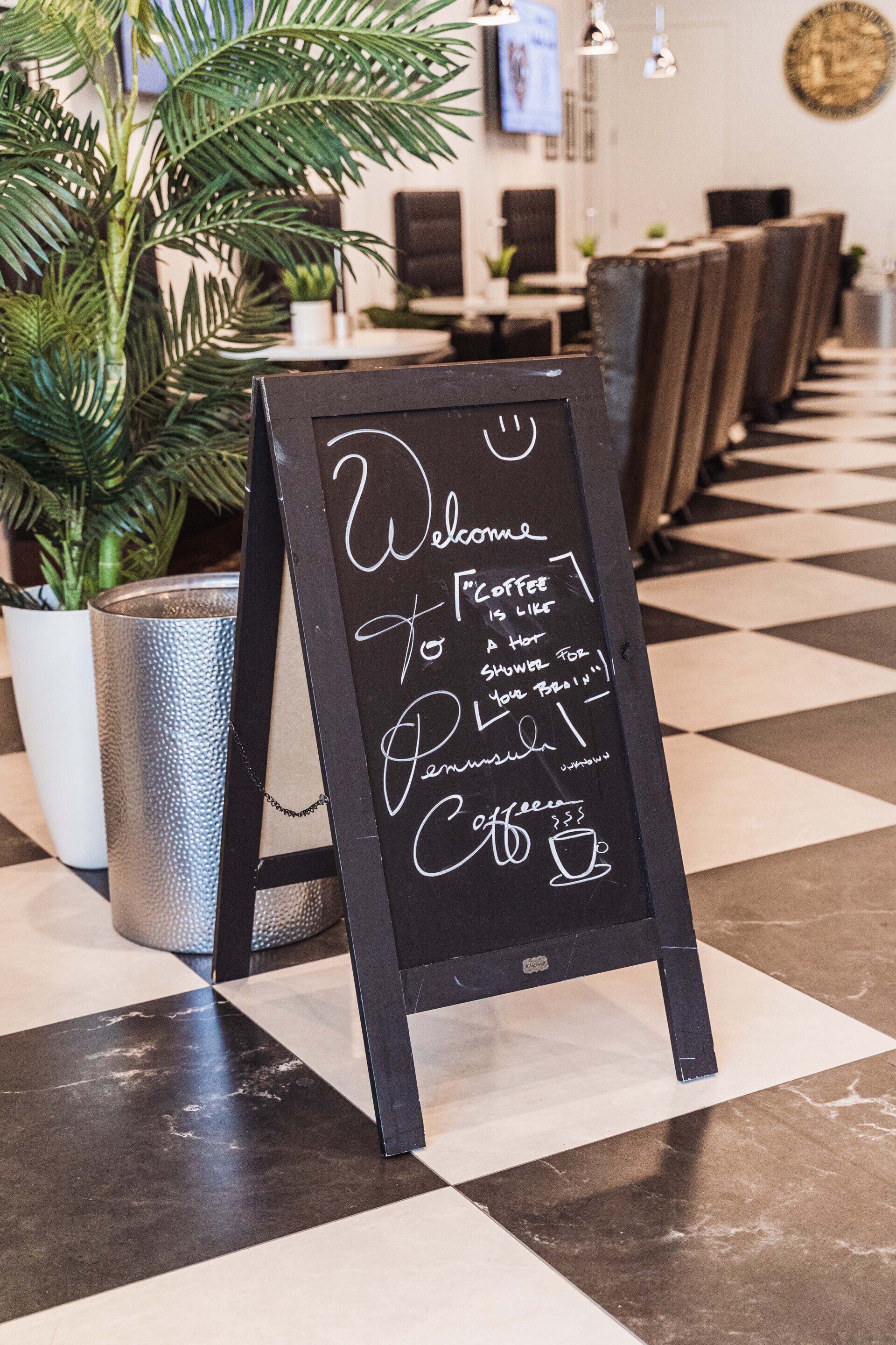 A chalkboard sign is sitting on a checkered floor in a restaurant.