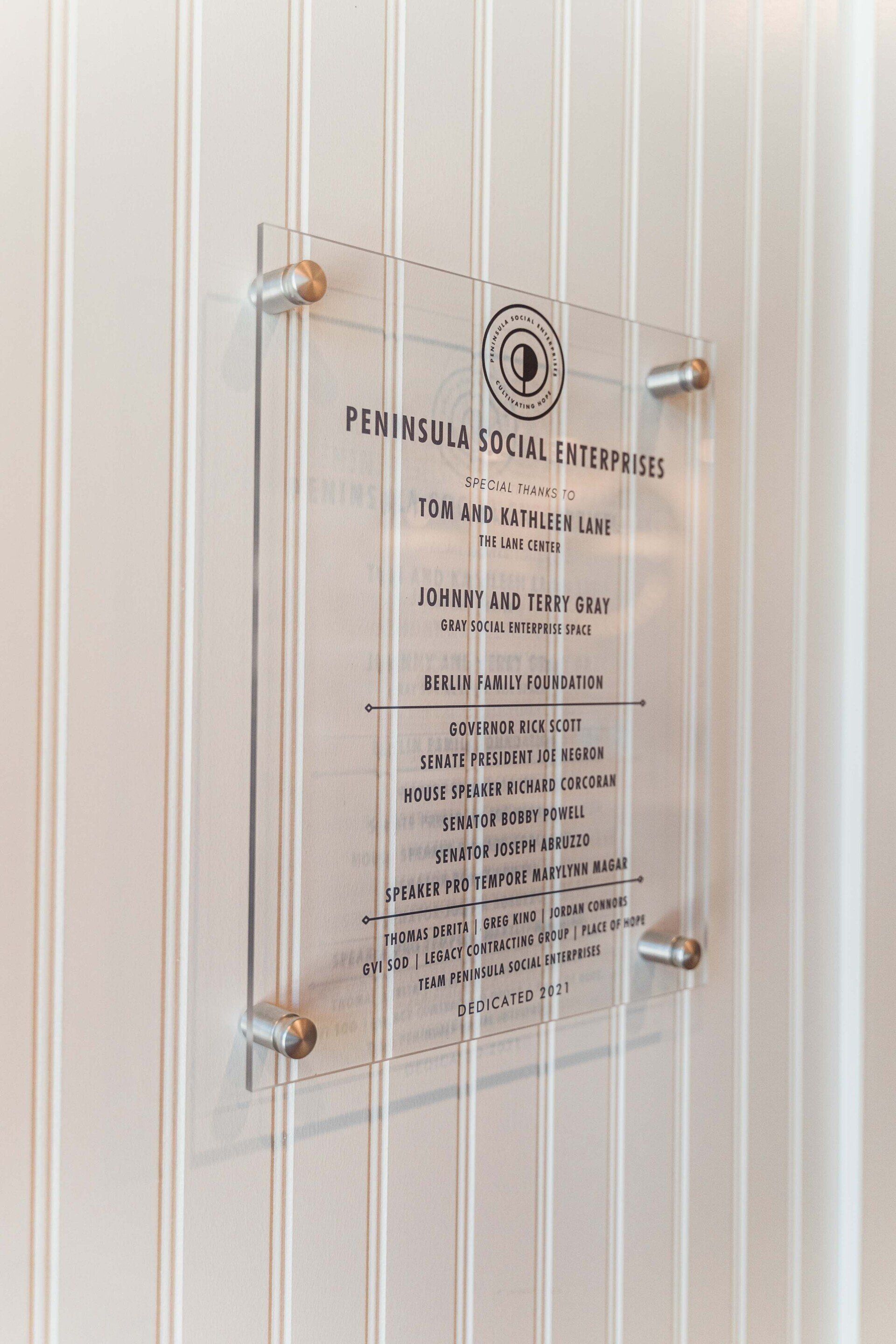 A clear sign is hanging on a white wall.