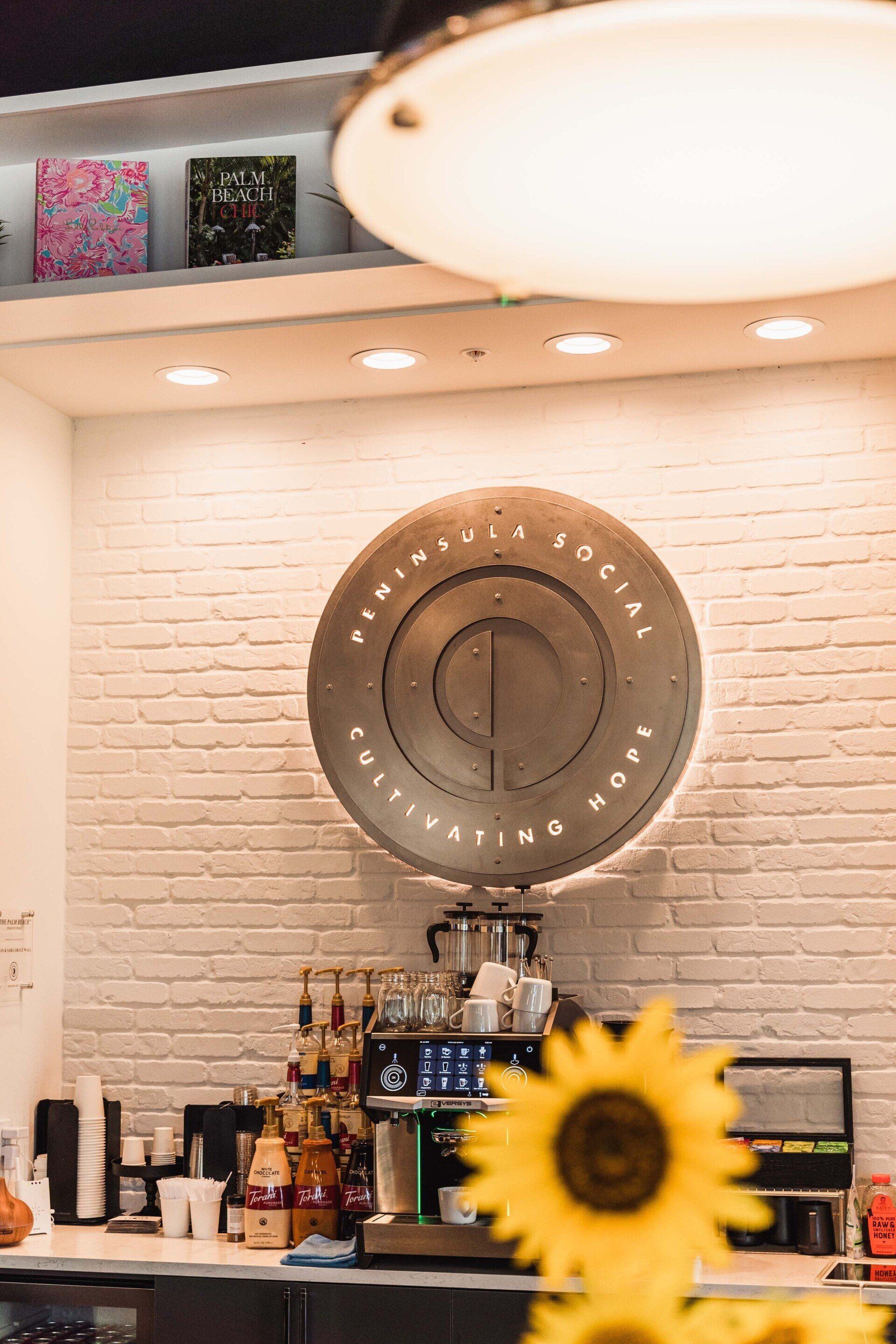 A sunflower is in the foreground of a restaurant with a clock on the wall.