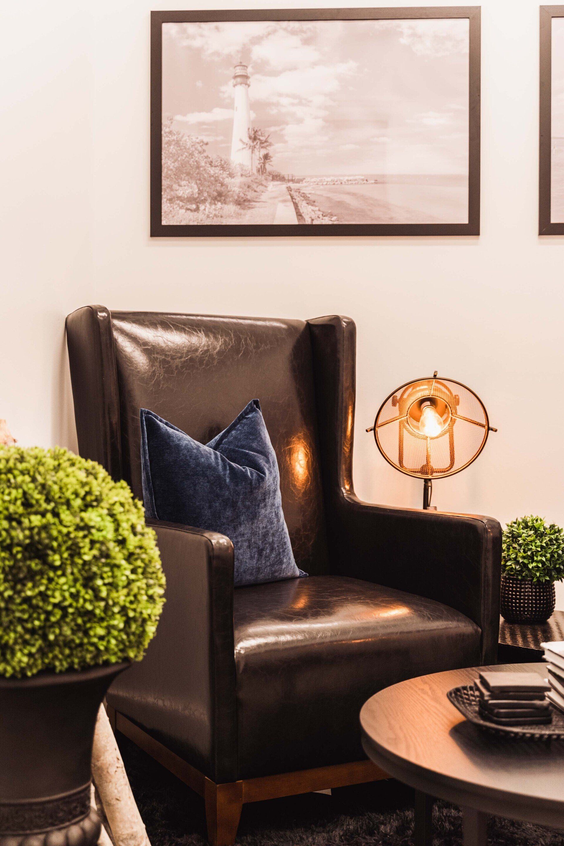 A black leather chair with a blue pillow is sitting in a living room next to a table.