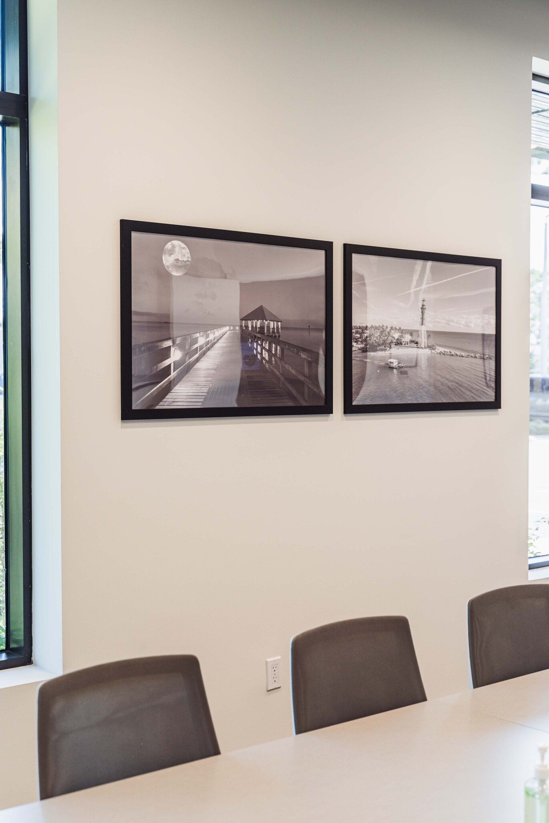 Two framed pictures are hanging on a wall above a conference table.