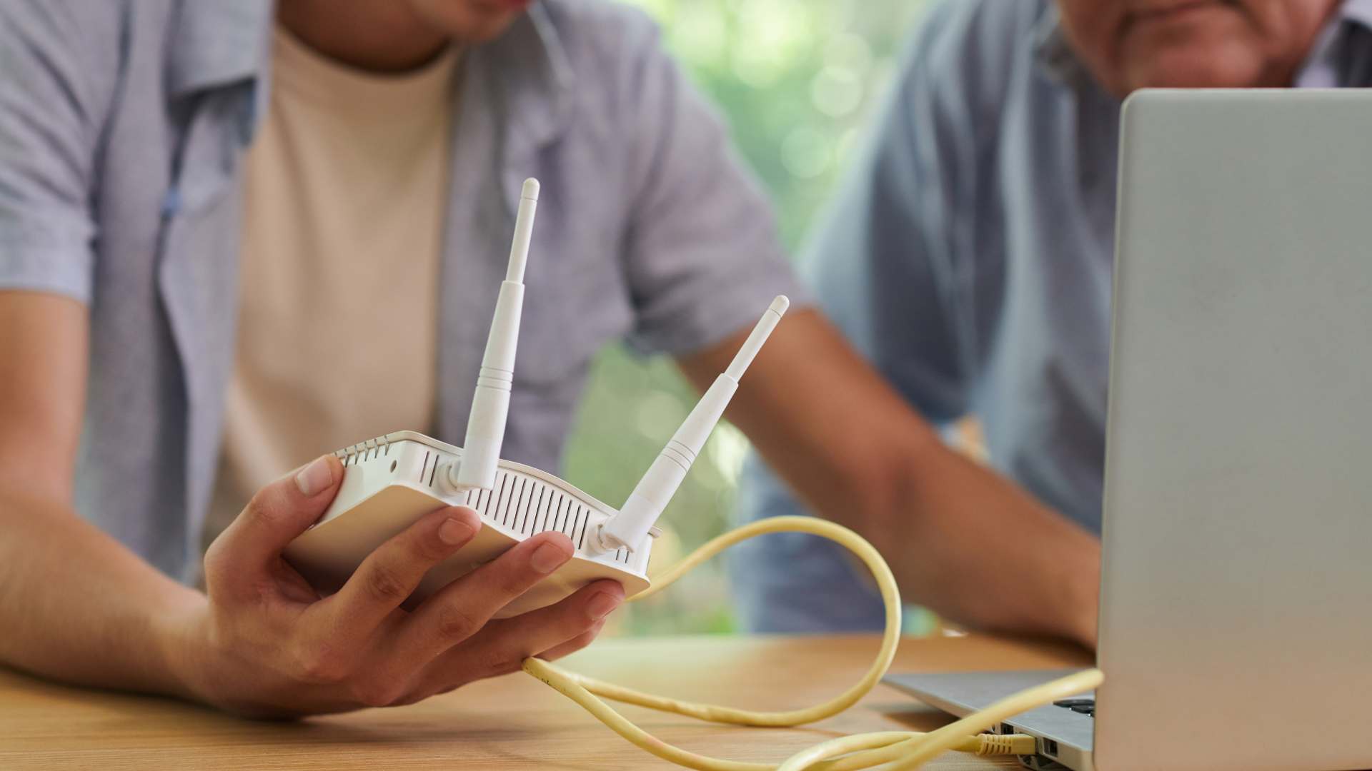 Two men are sitting at a table looking at a router.