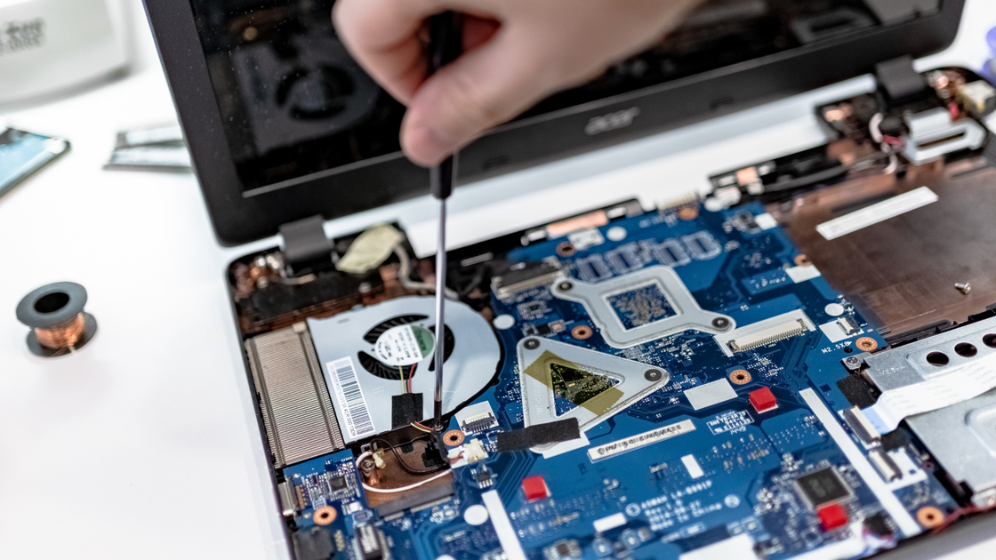 A person is fixing a laptop computer with a screwdriver.