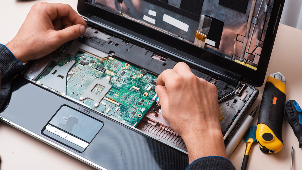 A person is repairing a laptop computer with tools on the table.