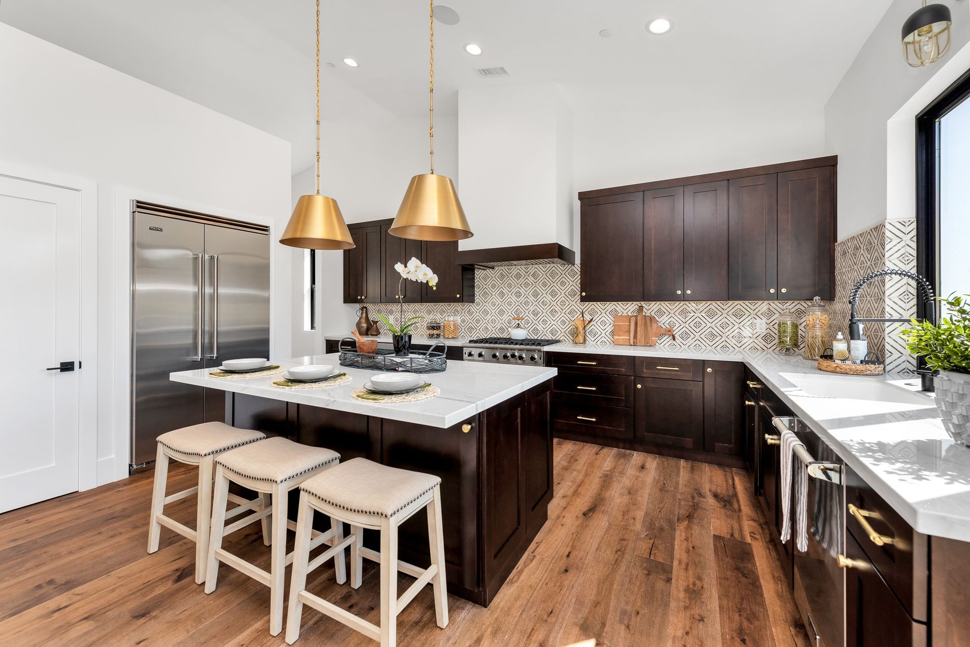 Modern kitchen with dark cabinets, white countertops, and gold pendant lights.