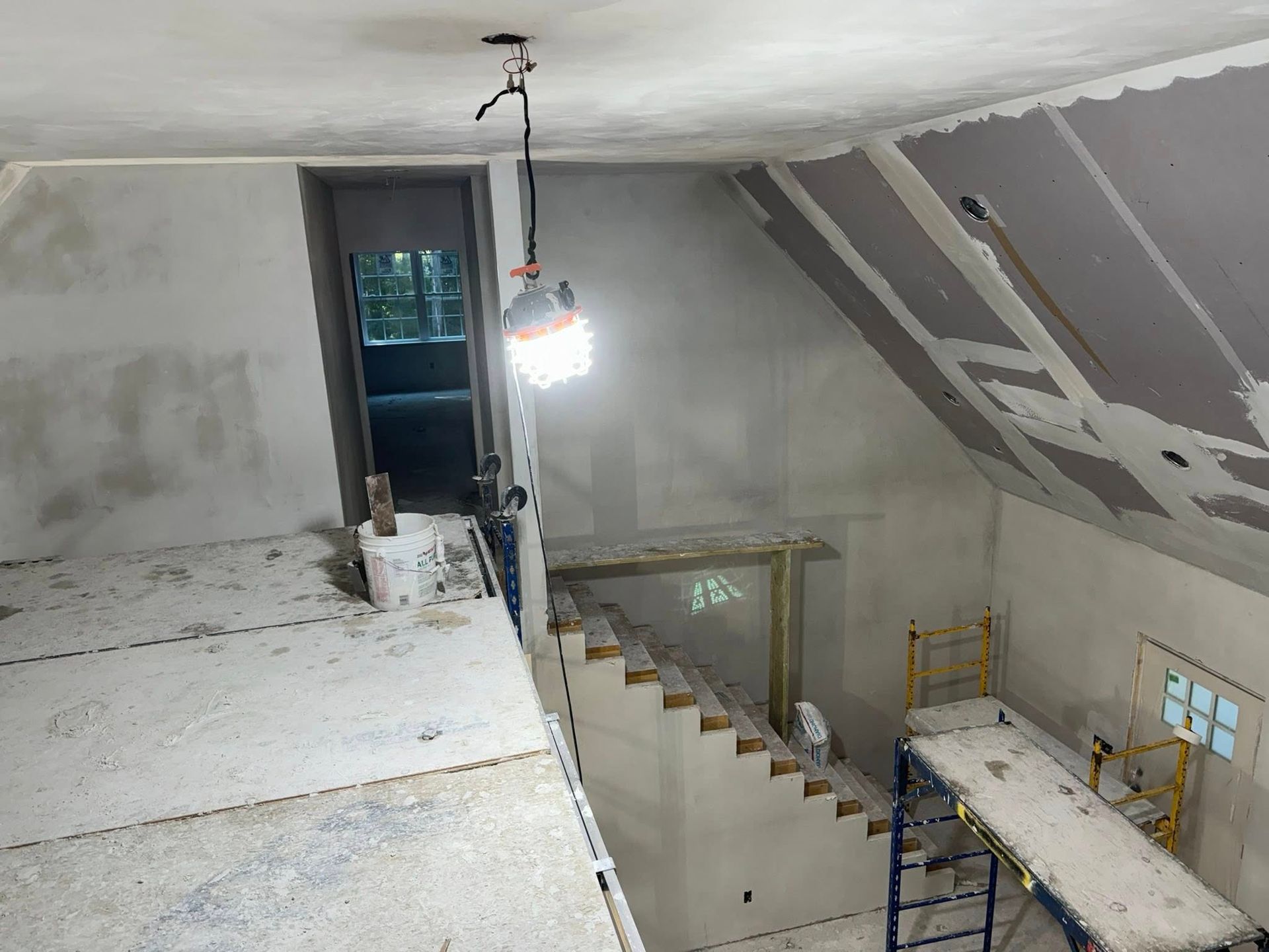 Interior of a room under construction with drywall and a temporary work light hanging.