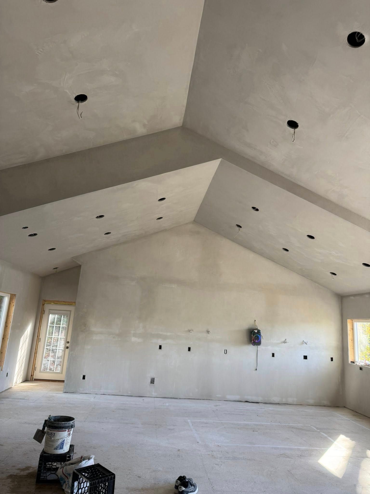 Large, light-colored room with unfinished walls and ceiling. Electrical outlets and recessed lights are visible.