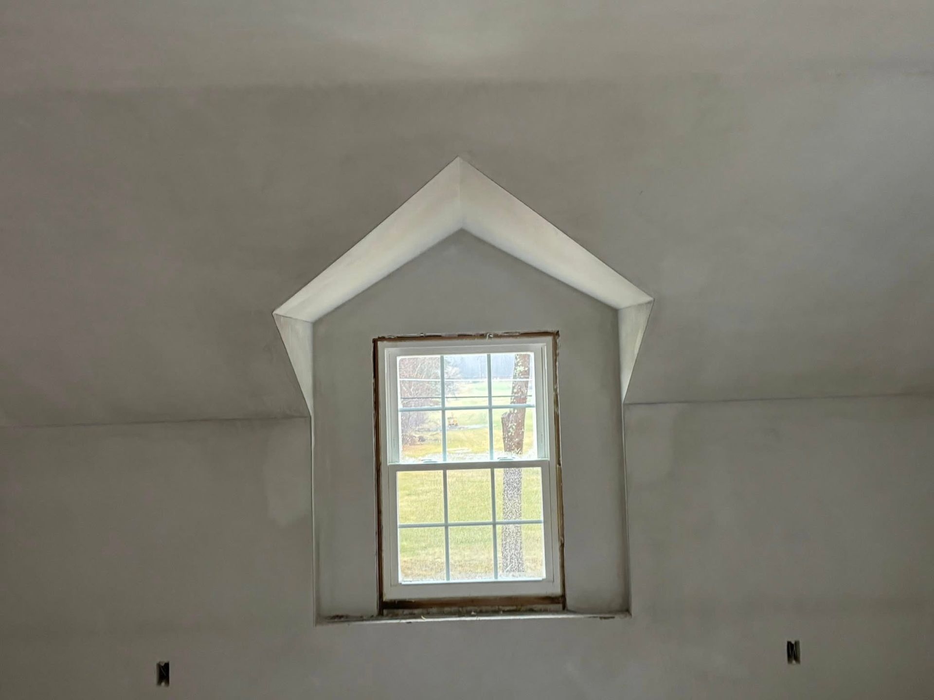 Interior view of a room with drywall installed on walls and ceiling, with taped seams and applied joint compound.