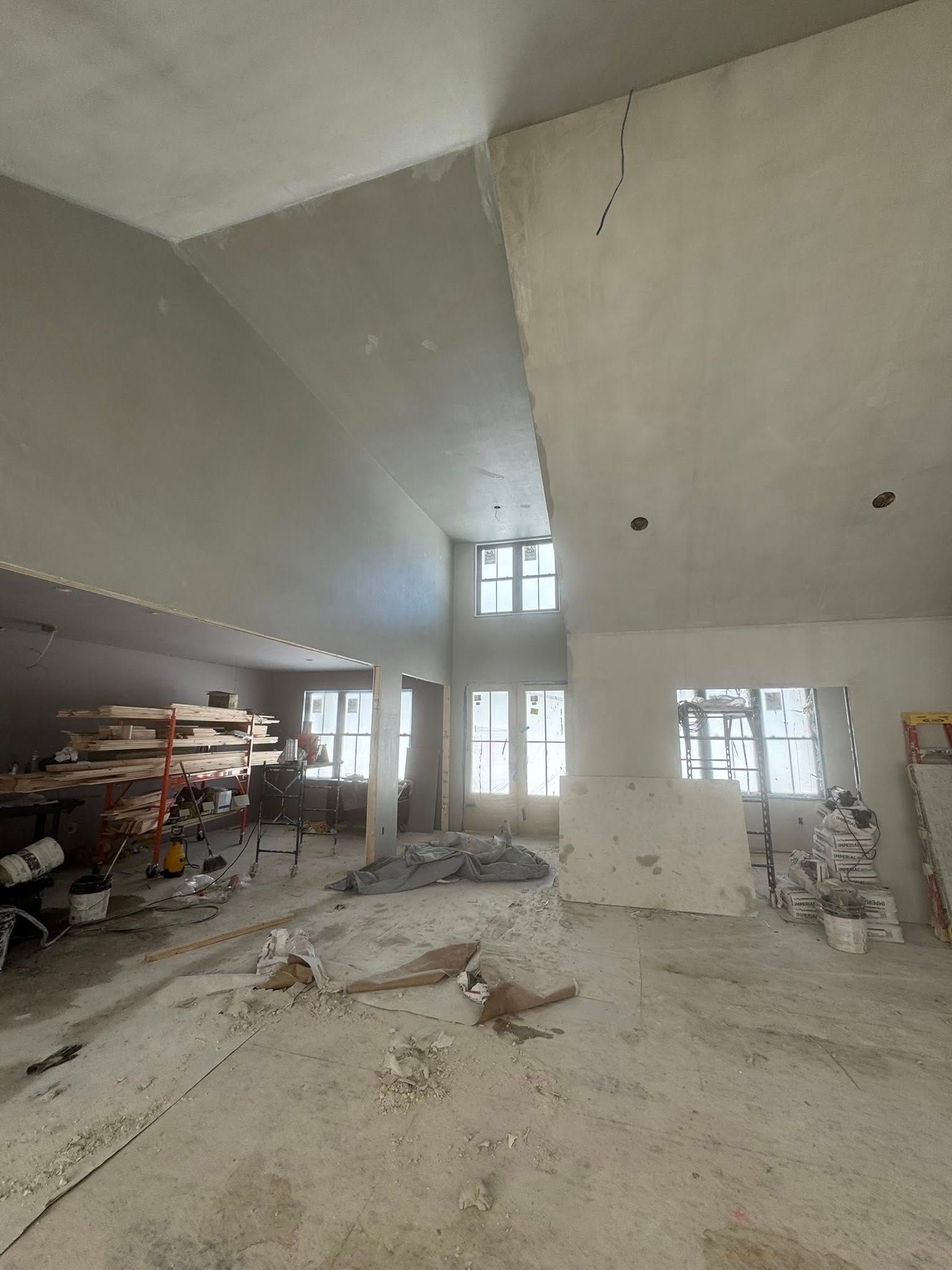 Interior of a room under construction, with high ceilings, unfinished walls, and scattered materials.