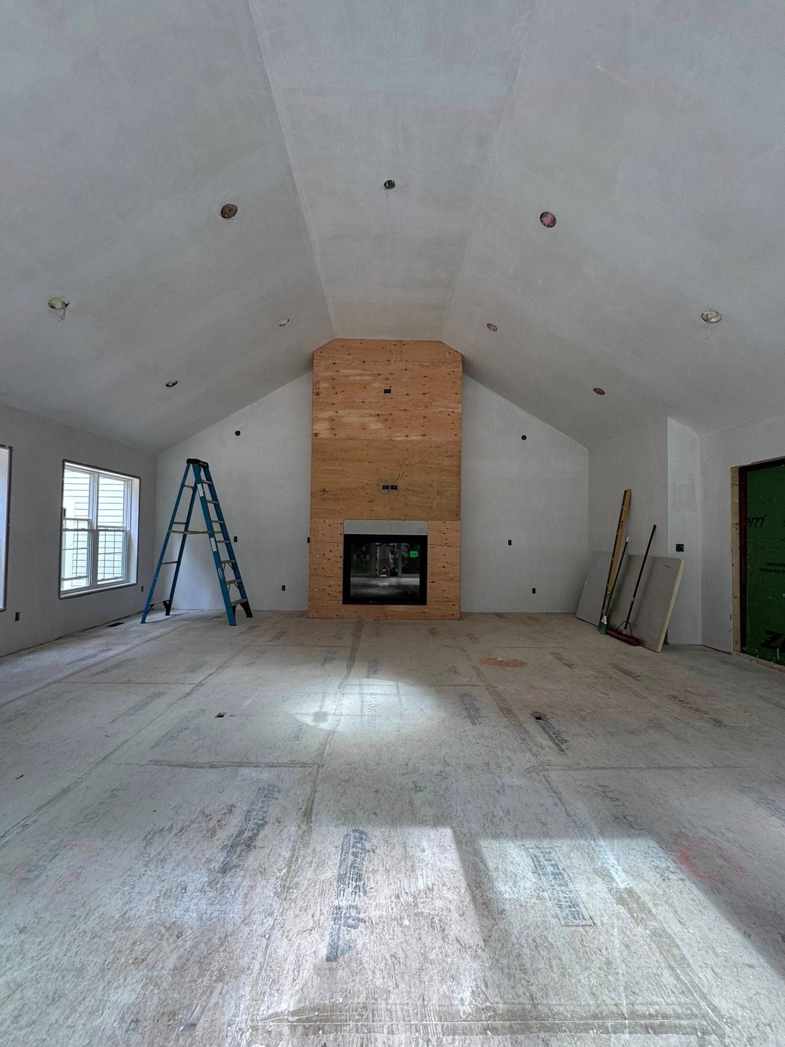 Interior of a room under construction with a fireplace, ladder, and exposed wood and drywall.
