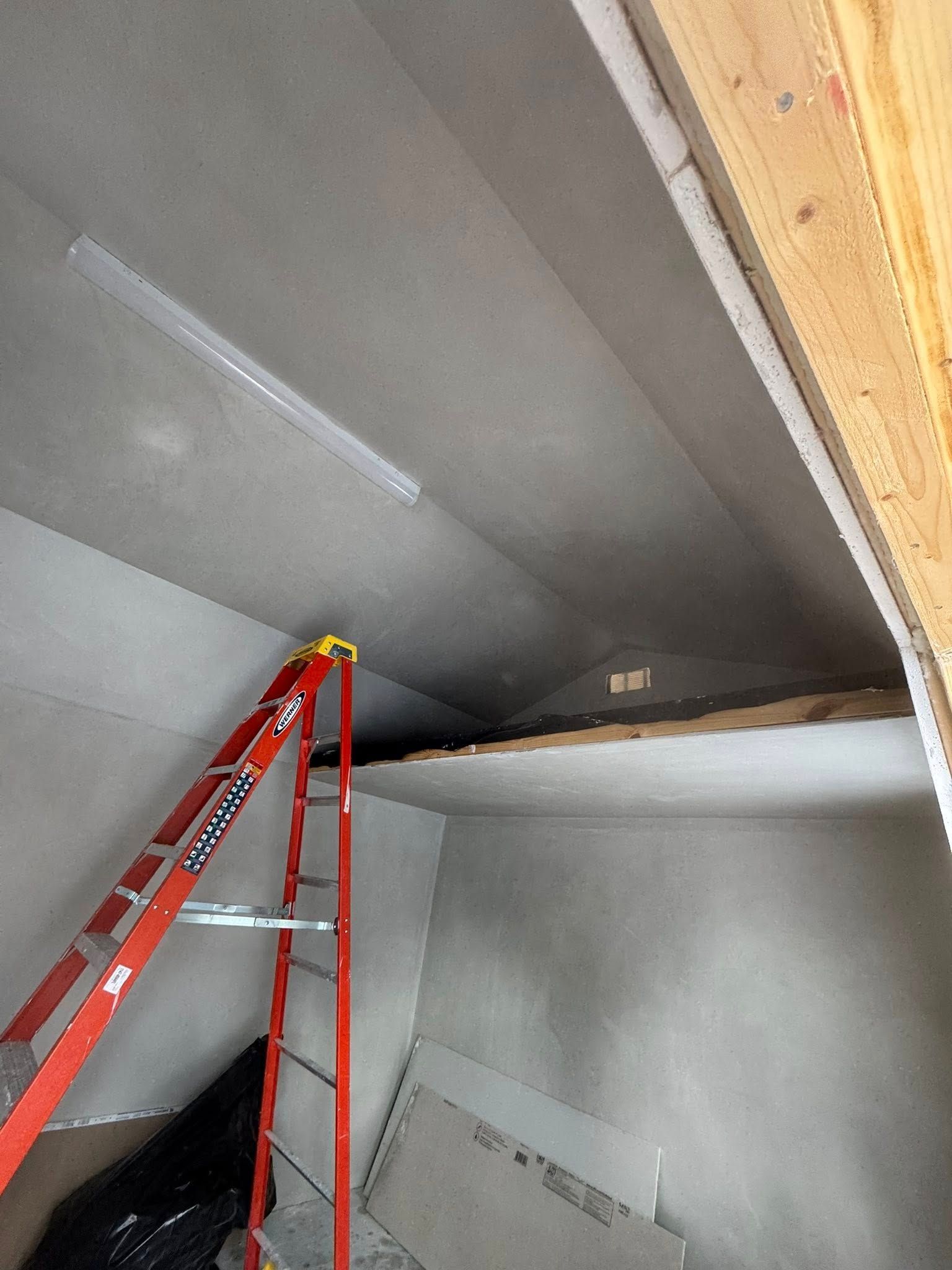 Red ladder inside a room under construction; drywall on walls and ceiling.