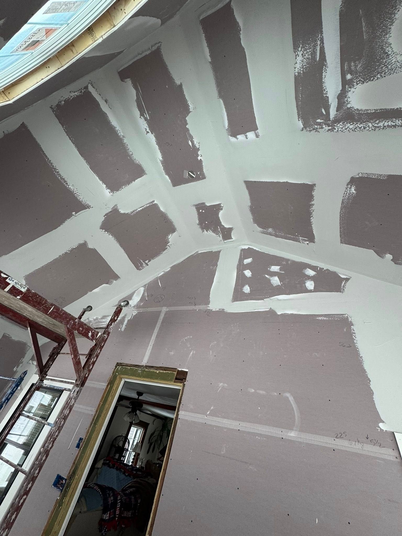 Interior view of a room with drywall installed on walls and ceiling, with taped seams and applied joint compound.