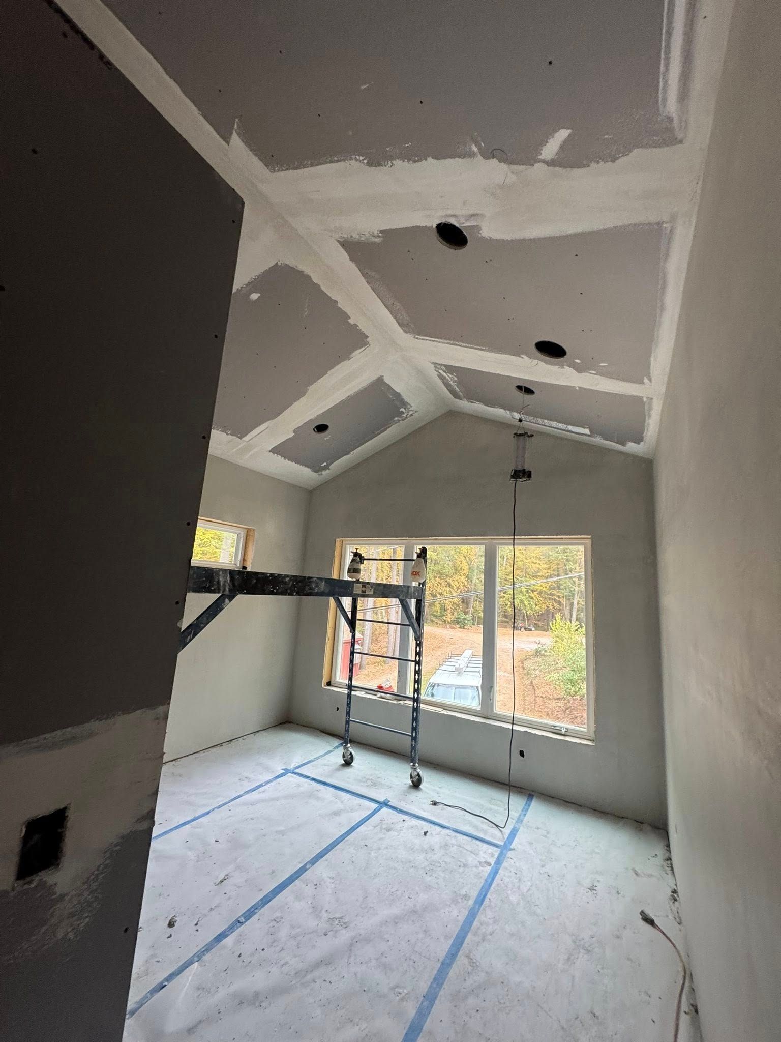 Interior of a house under construction; white walls, vaulted ceiling, orange ladder in foreground, construction materials on the floor. Interior of a house under construction; white walls, vaulted ceiling, orange ladder in foreground, construction materials on the floor.