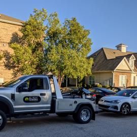 A tow truck hooking up a white car, in front of an apartment building on a sunny day.