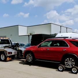 A red SUV being towed by a tow truck on a sunny day in front of a white building.