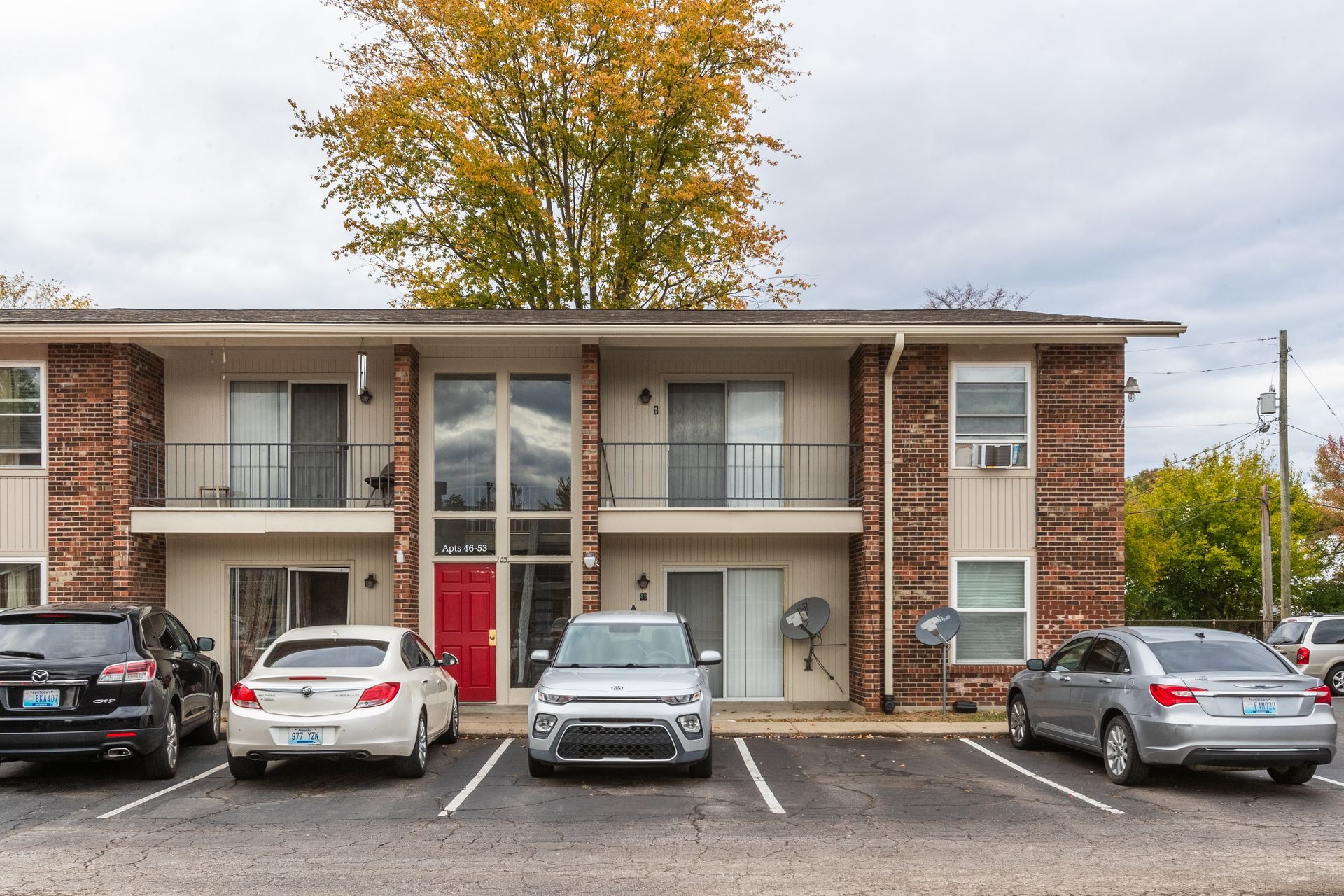 A row of cars are parked in front of a large apartment building.