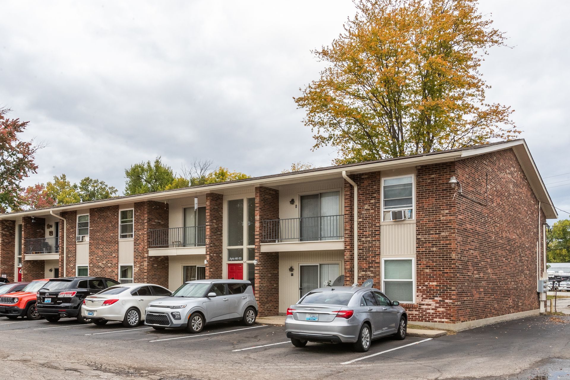 A row of cars are parked in front of a brick apartment building.