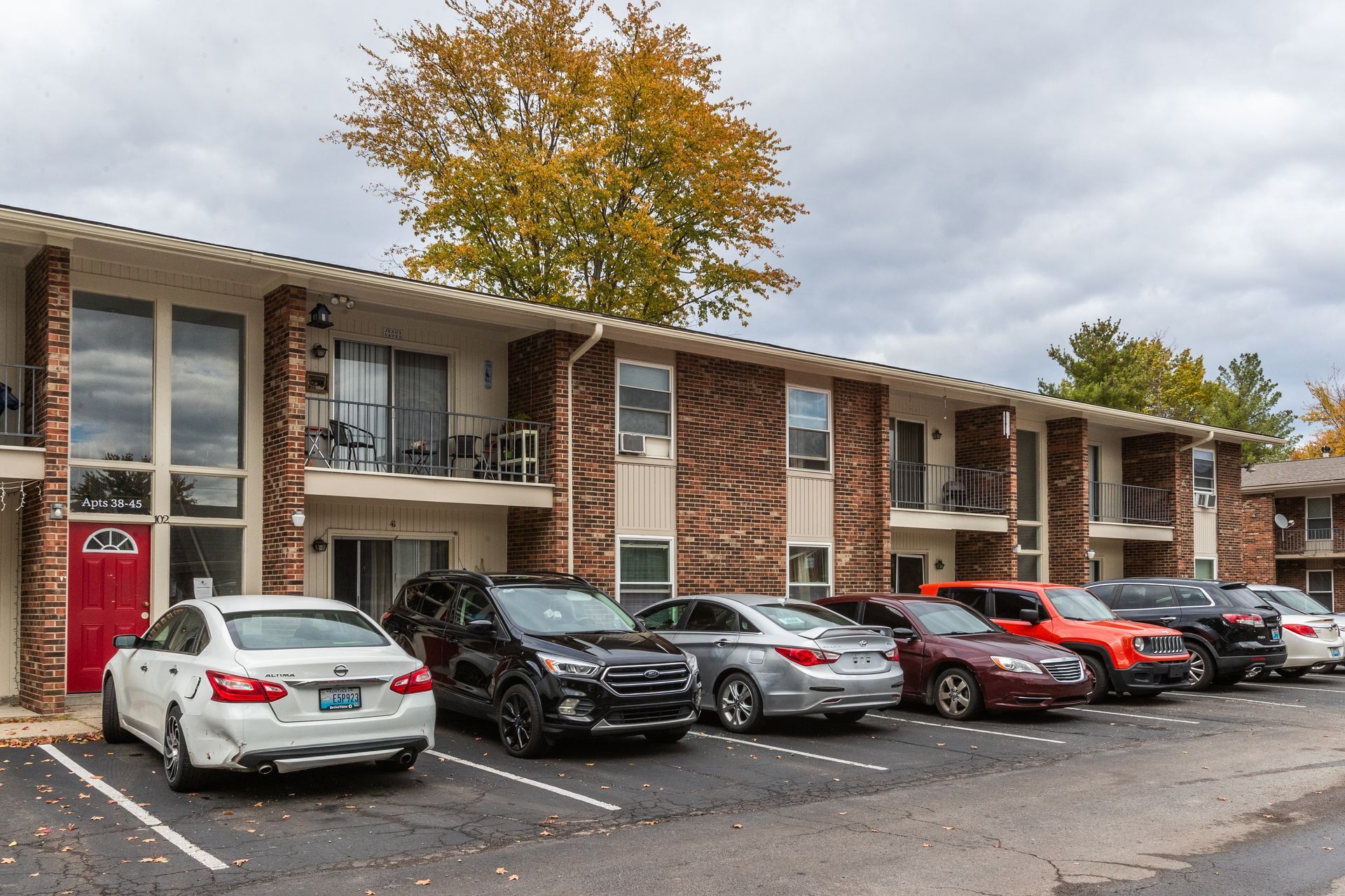 A row of cars are parked in front of a apartment building.